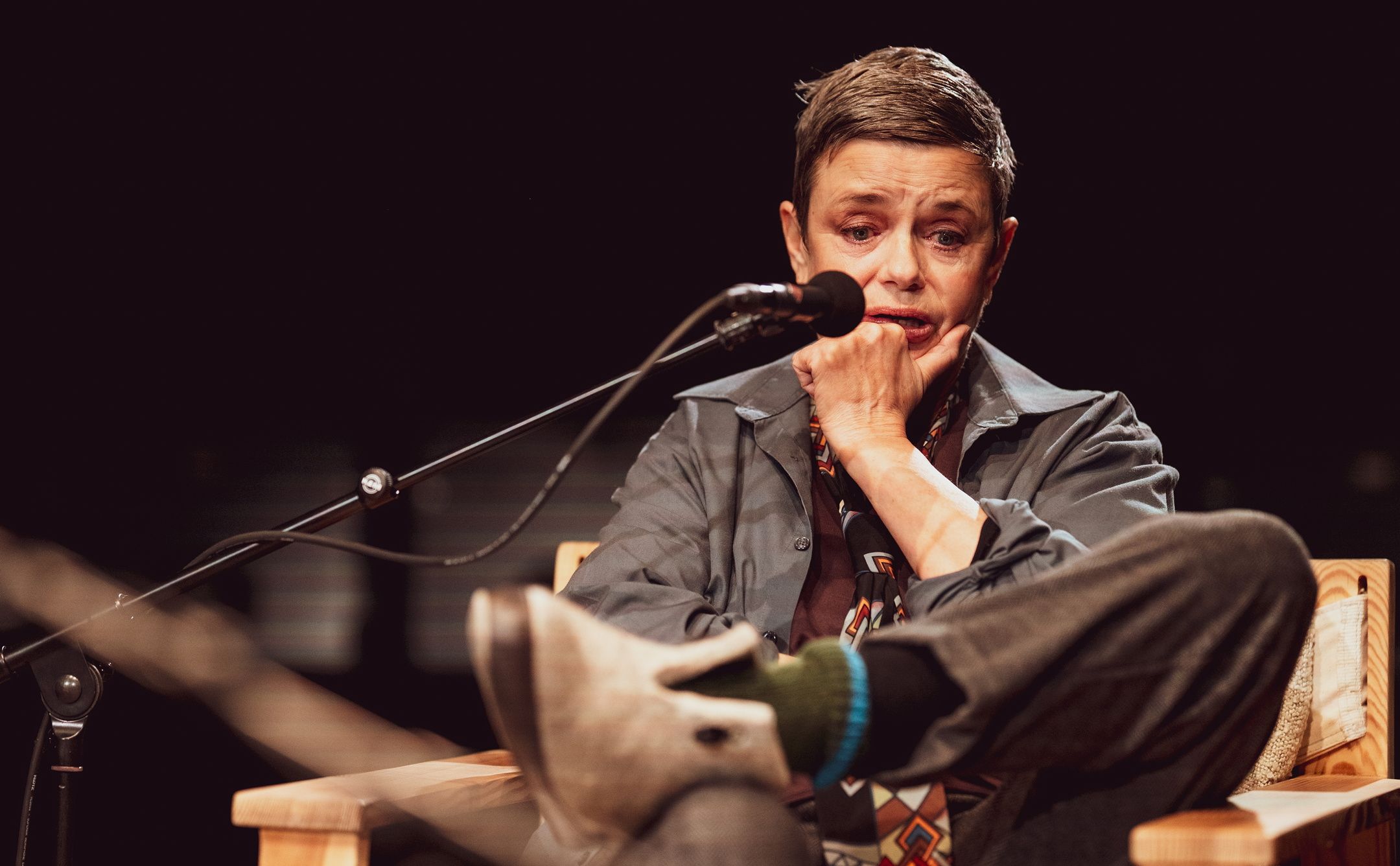 Person med kort hår sitter tankefullt med hånden mot haken og foten hvilende på stolarmen.