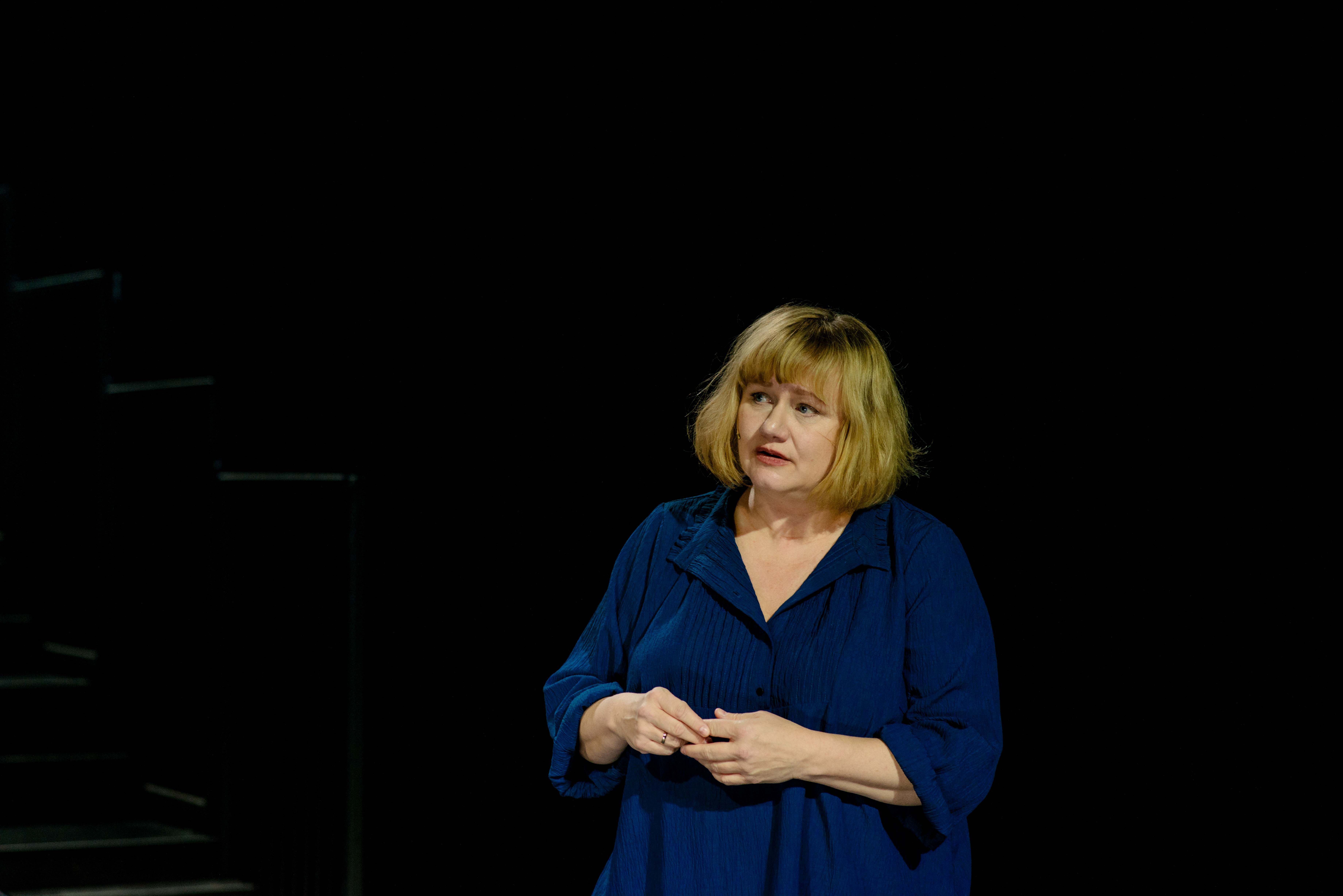 Kvinne står og ser usikker ut på mørk scene