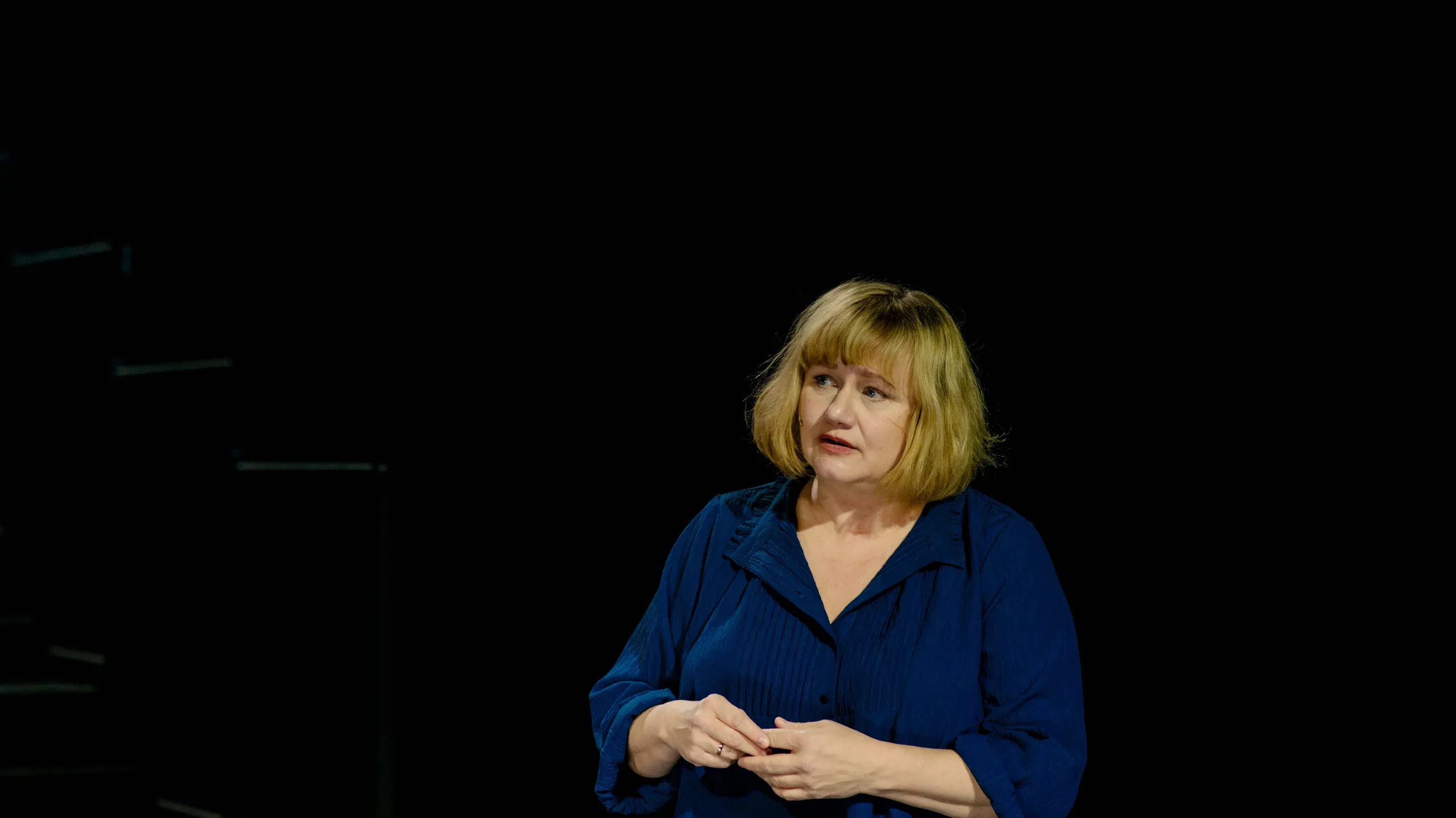 Kvinne står og ser usikker ut på mørk scene