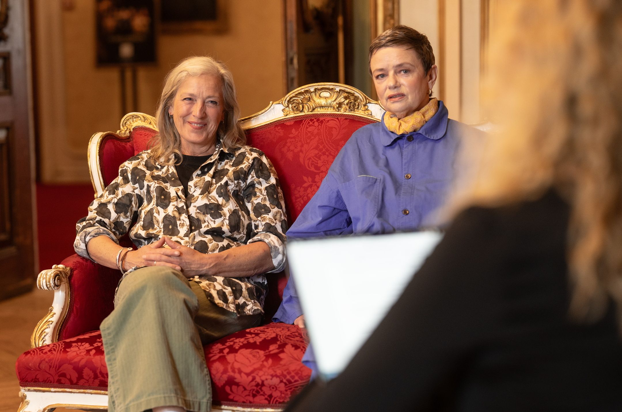 To kvinner i intervjusetting i rød rokokkosofa