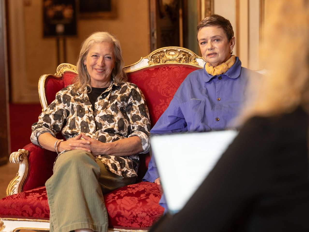 To kvinner i intervjusetting i rød rokokkosofa
