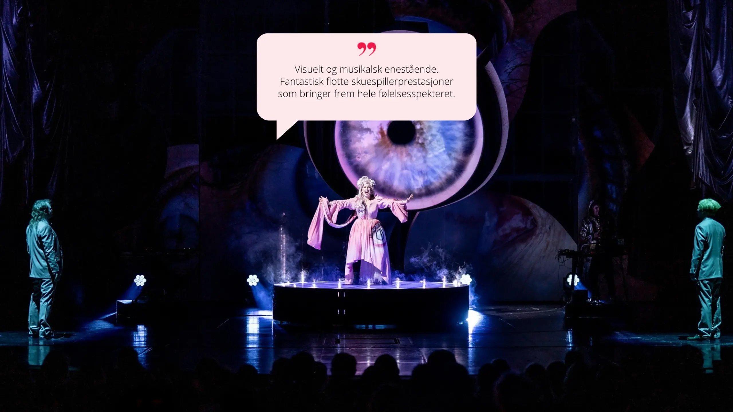 karakteren står alene på en rund plattform med røyk- og lyseffekter. Den store øyeprojeksjonen er også her i bakgrunnen, og stemningen er eventyrlig og visjonær.  Sitat i snakkeboble:  "Visuelt og musikalsk enestående. [...] hele følelsesspekteret."