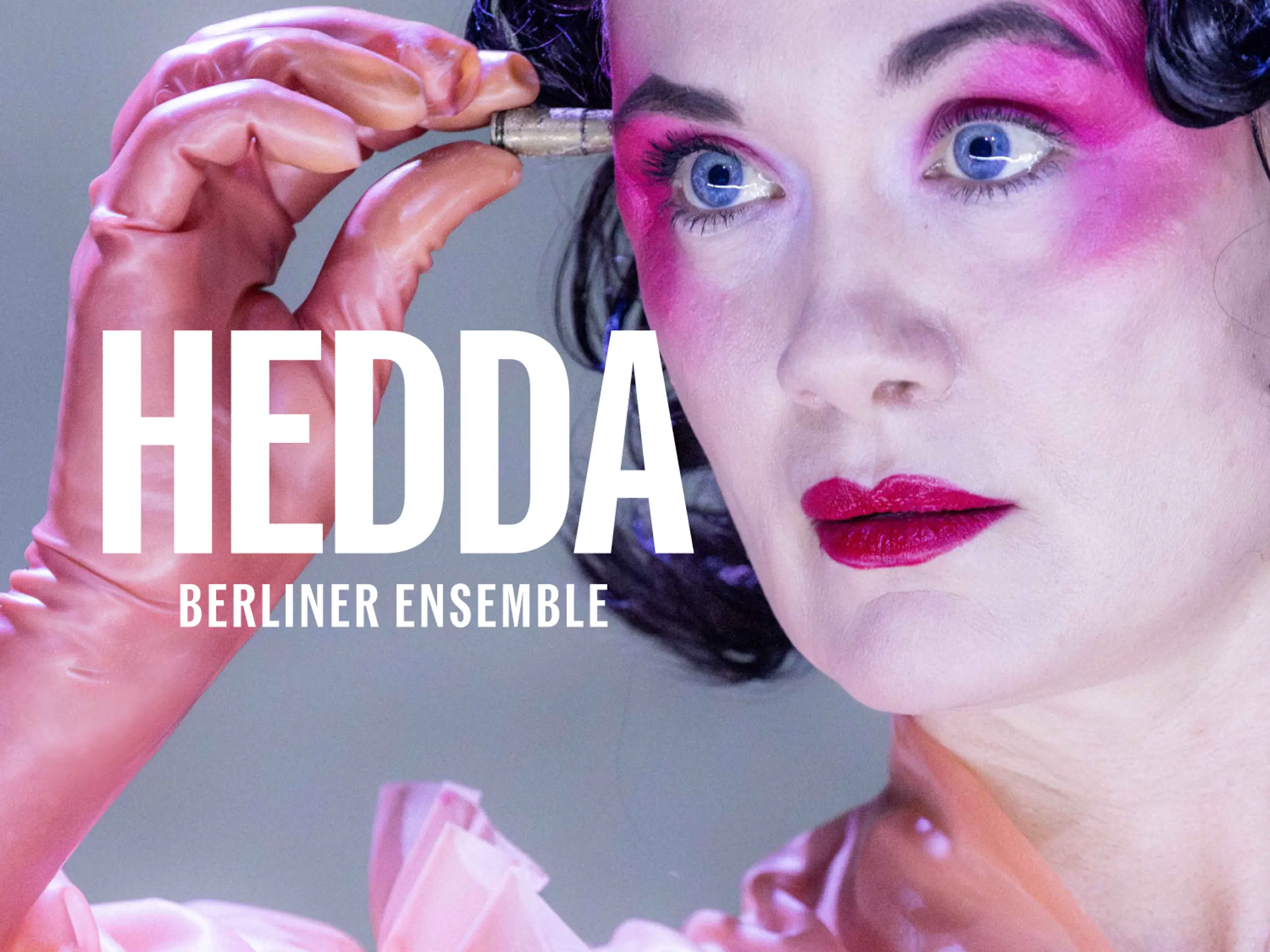Person med kort mørkt hår, kraftig rosa øyenskygge og ferskenfarget kjole holder en liten patron foran pannen. Med tekst "Hedda - Berlioner ensemble"