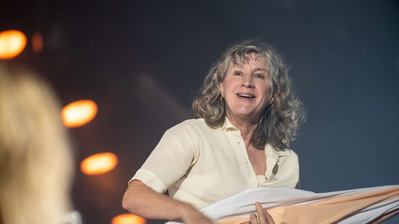 Smilende kvinne med grått hår holder sammenbrettet parasoll under varmt scenelys