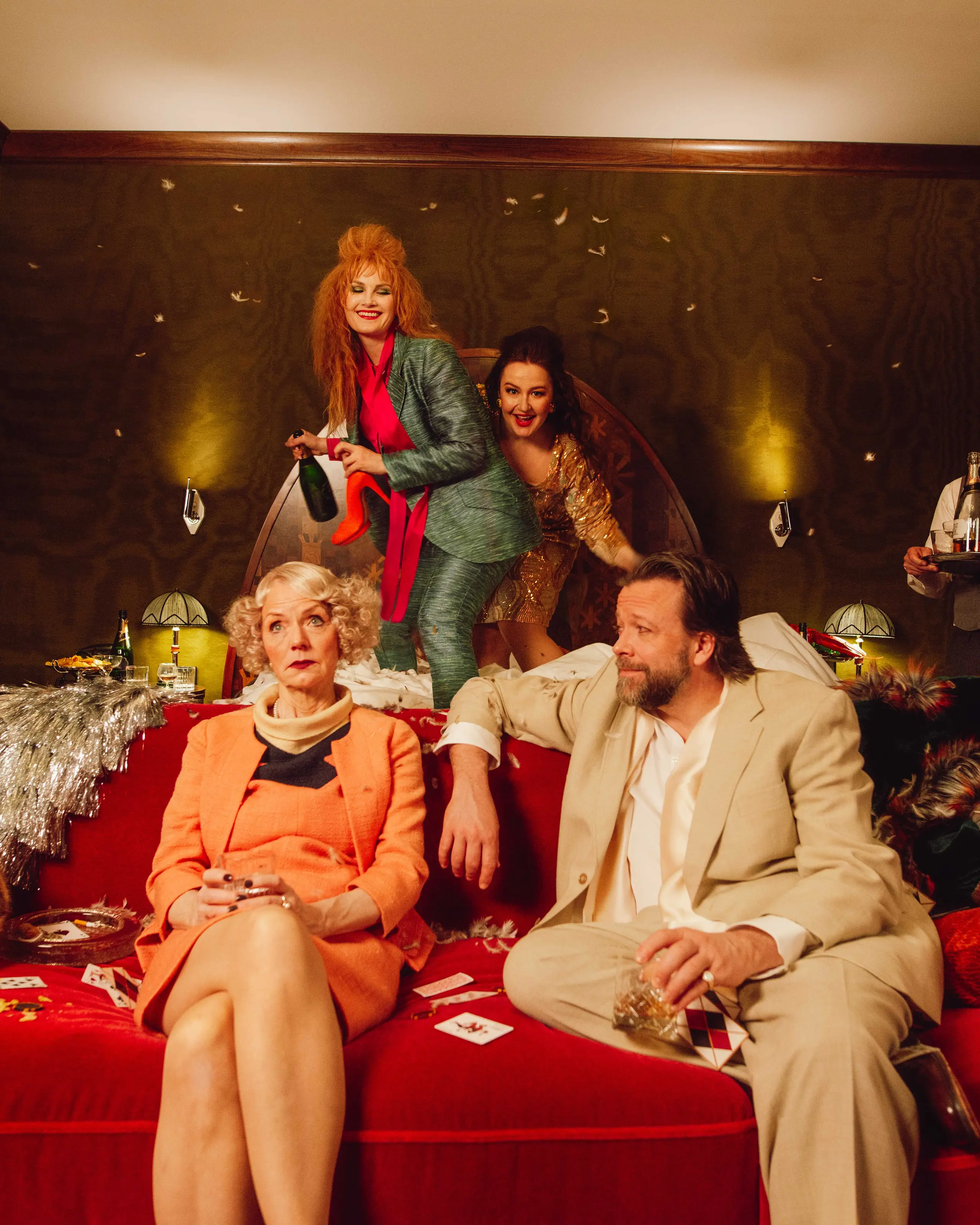 Fire skuespillere som herjer på et hotellrom. To kvinner hopper i senga, mens en kvinne og en mann sitter i sofaen