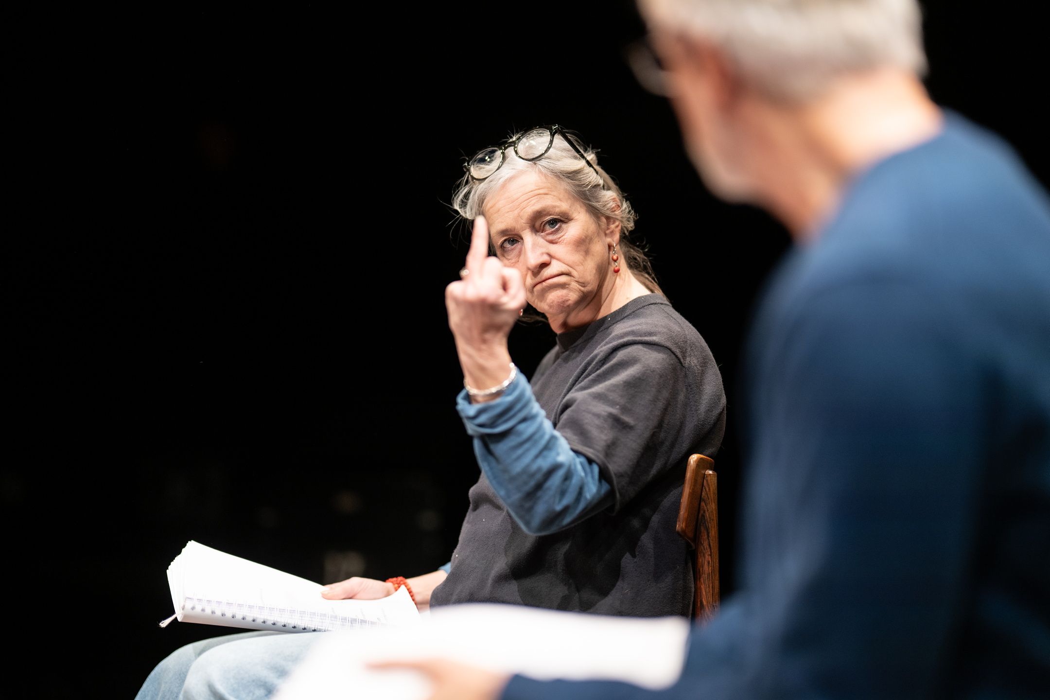 kvinne med grått hår i hestehale holder opp langfingeren mens hun ser alvorlig på en mann utenfor fokus.