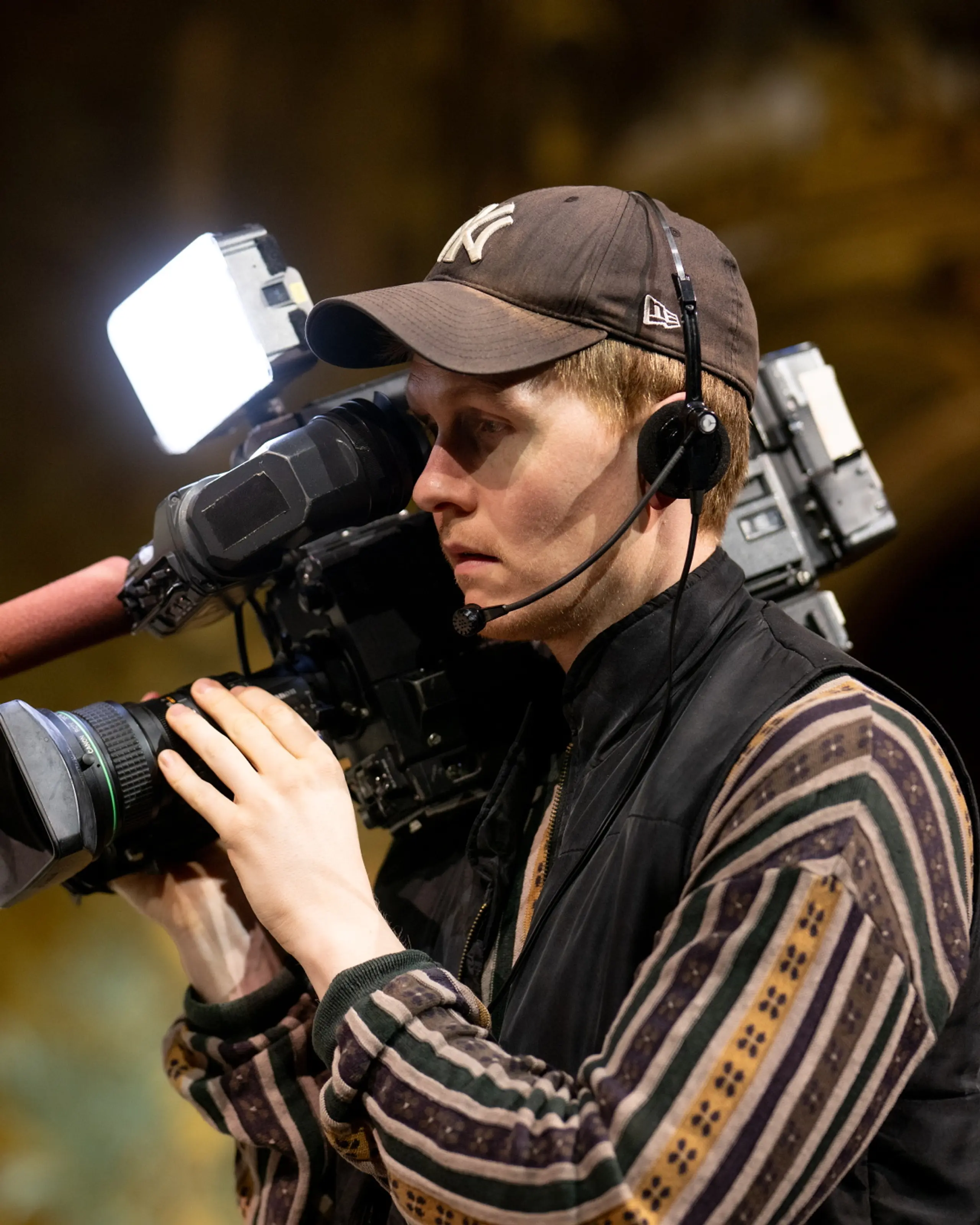 Person med caps og headset filmer med stort videokamera med lys og mikrofon i teatersal