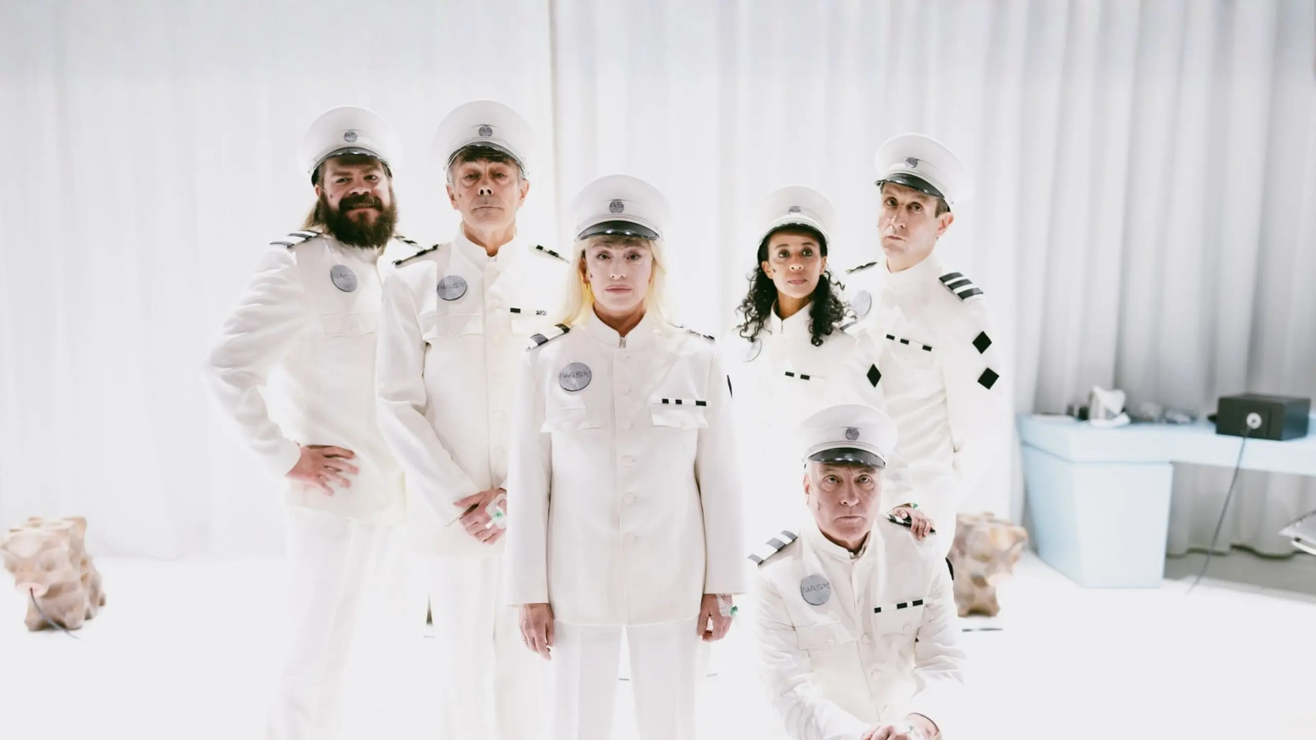 Seks personer i hvite futuristiske kostymer stilt opp til gruppebilde