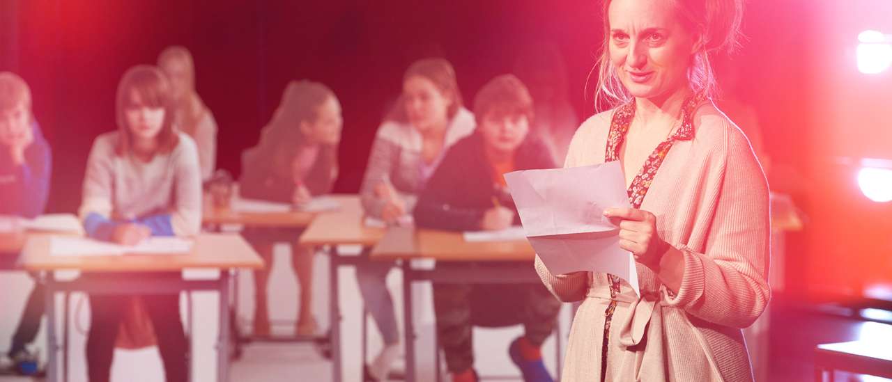 Kvinne i 30-årene står foran en klasse og holde noen papirer.