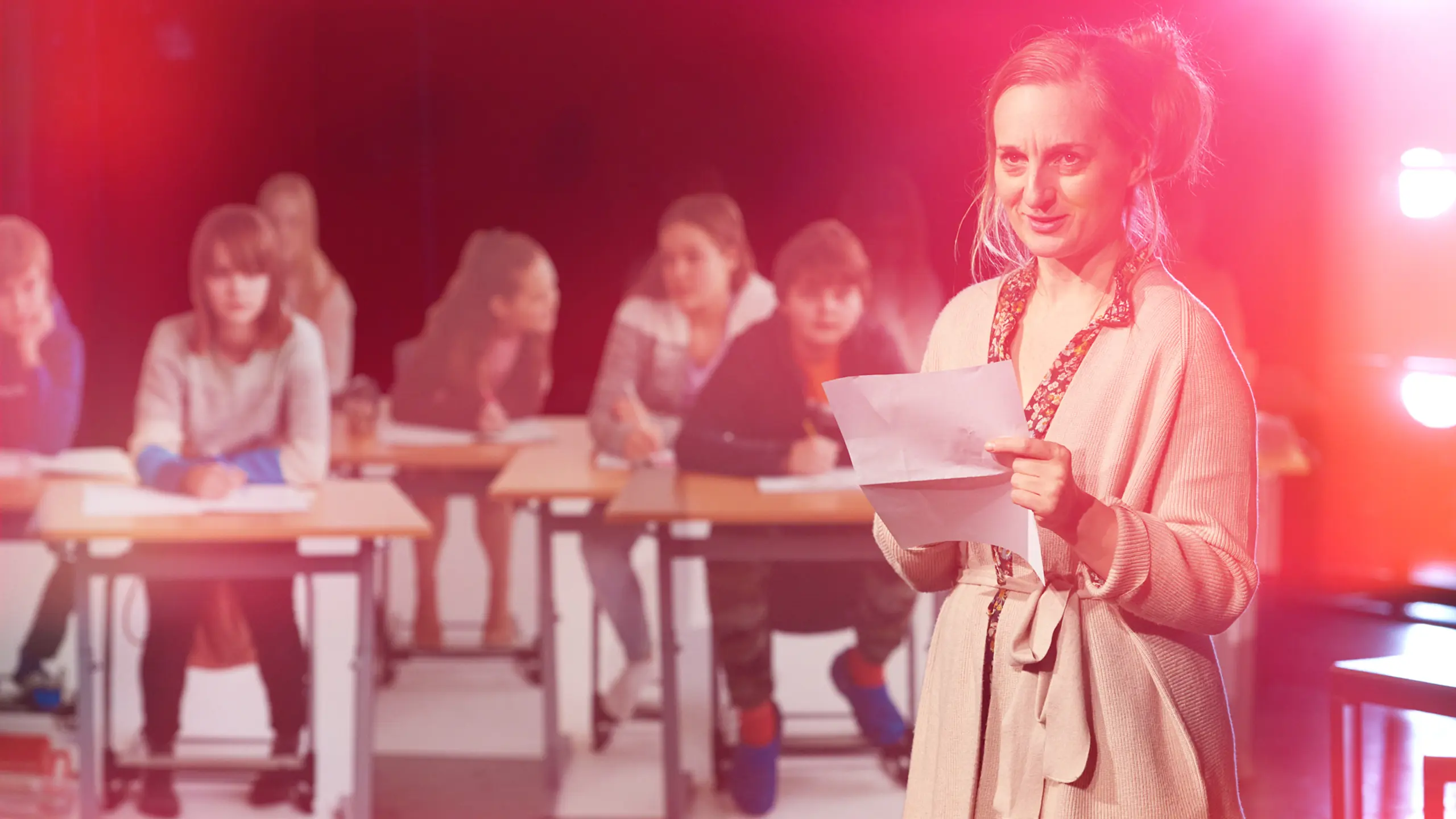 Kvinne i 30-årene står foran en klasse og holde noen papirer.