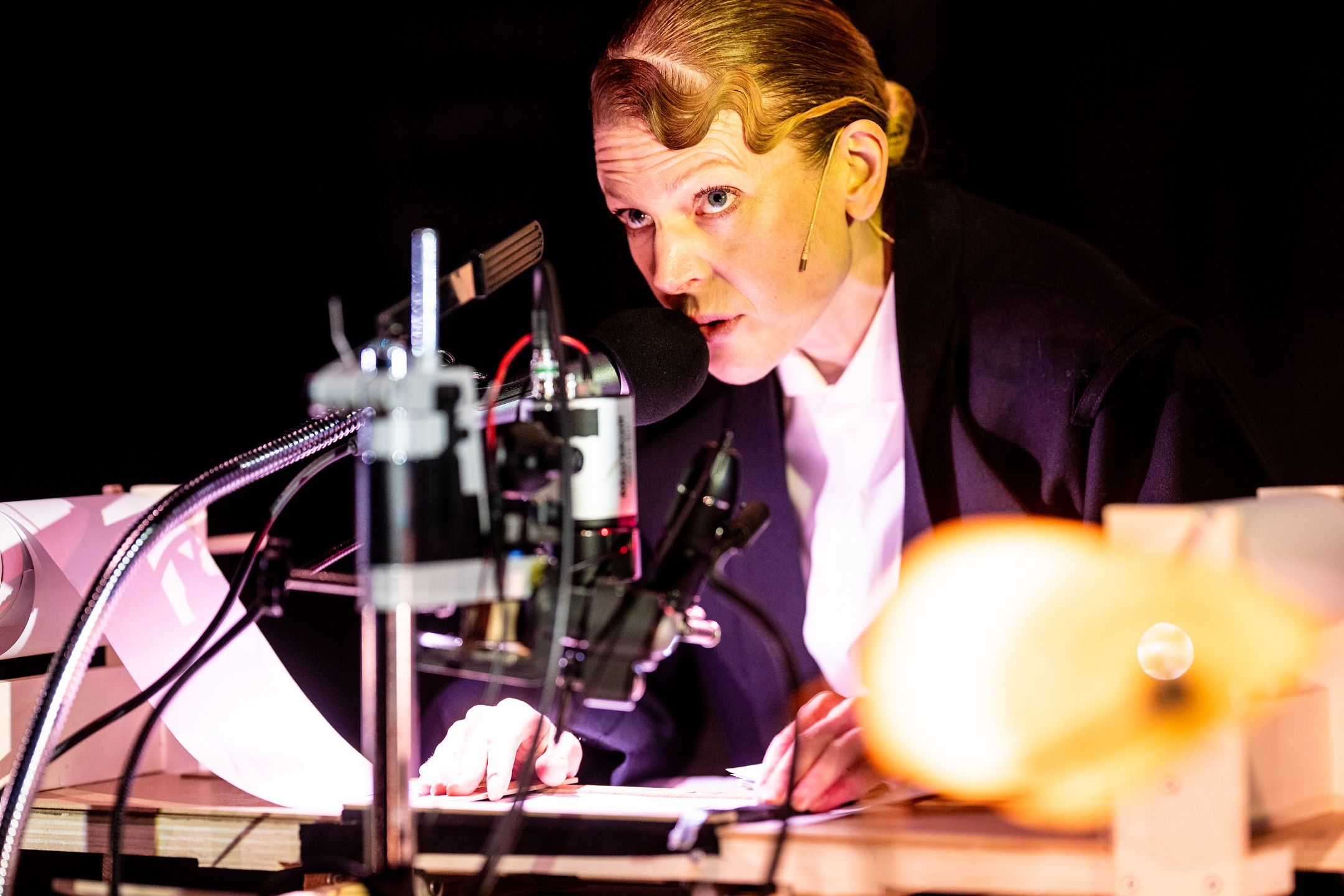 Kvinne snakker i mikrofon mens hun ruller på en liten papirrull under en lupe