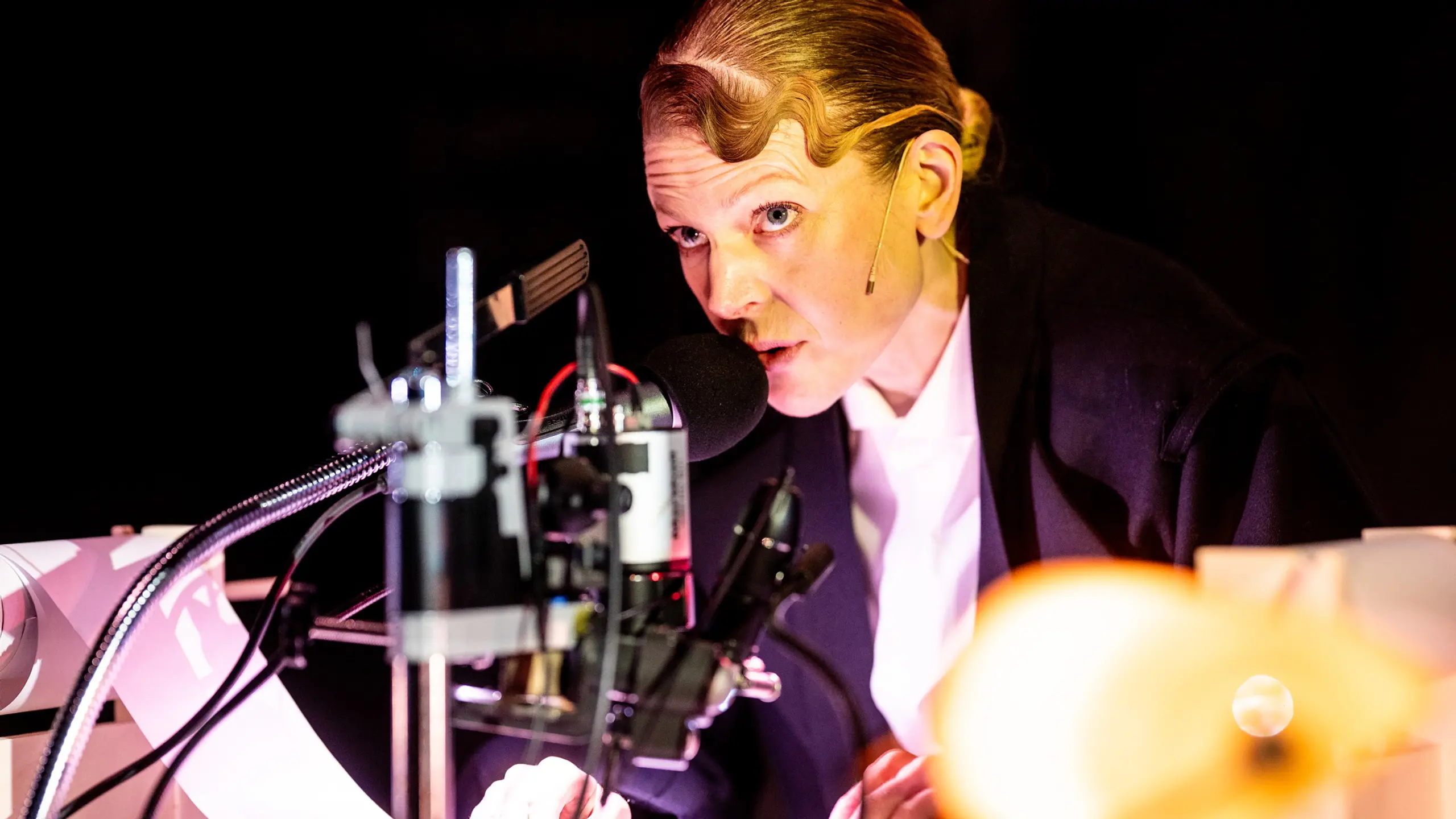 Kvinne snakker i mikrofon mens hun ruller på en liten papirrull under en lupe