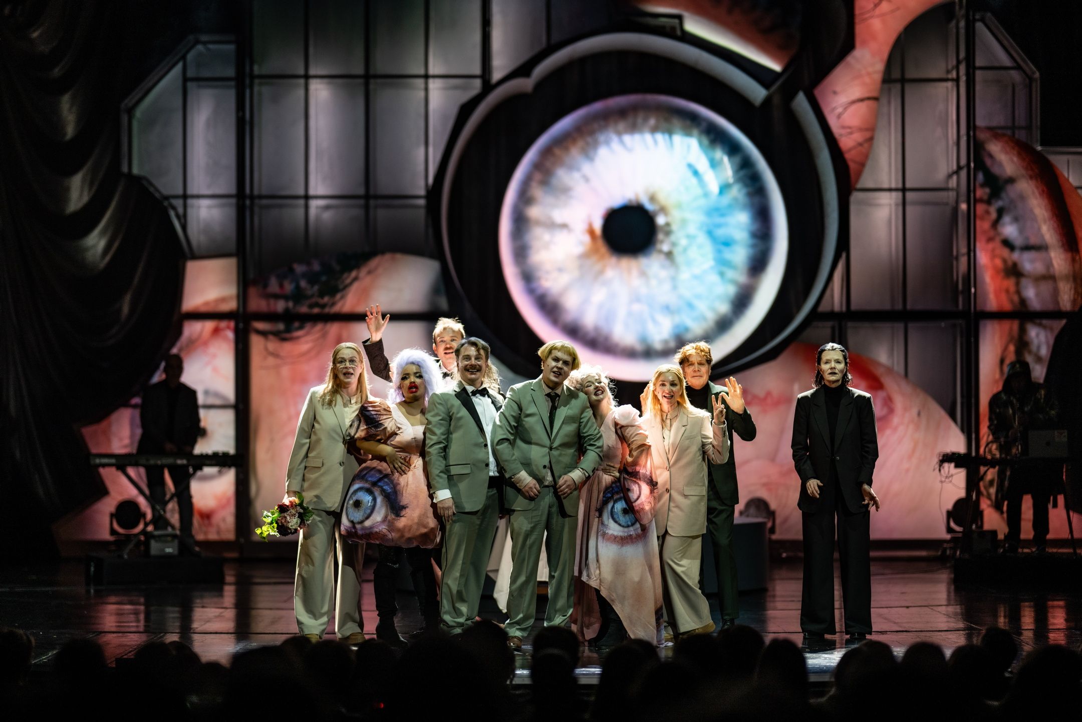 En gruppe skuespillere på en scene med et stort øye i kostyme og på bakvegg