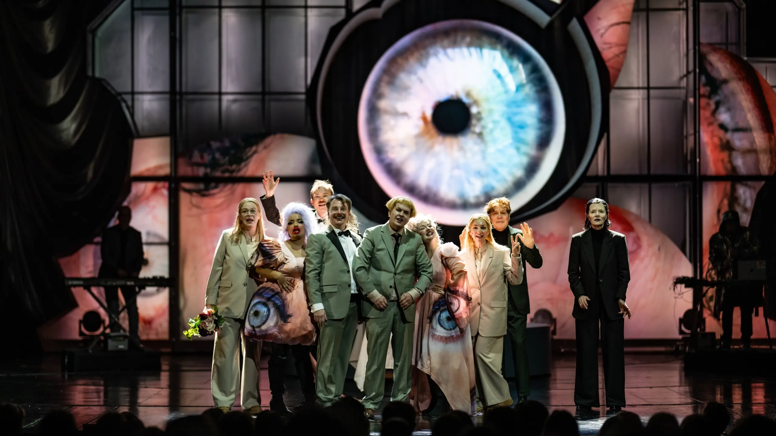 En gruppe skuespillere på en scene med et stort øye i kostyme og på bakvegg