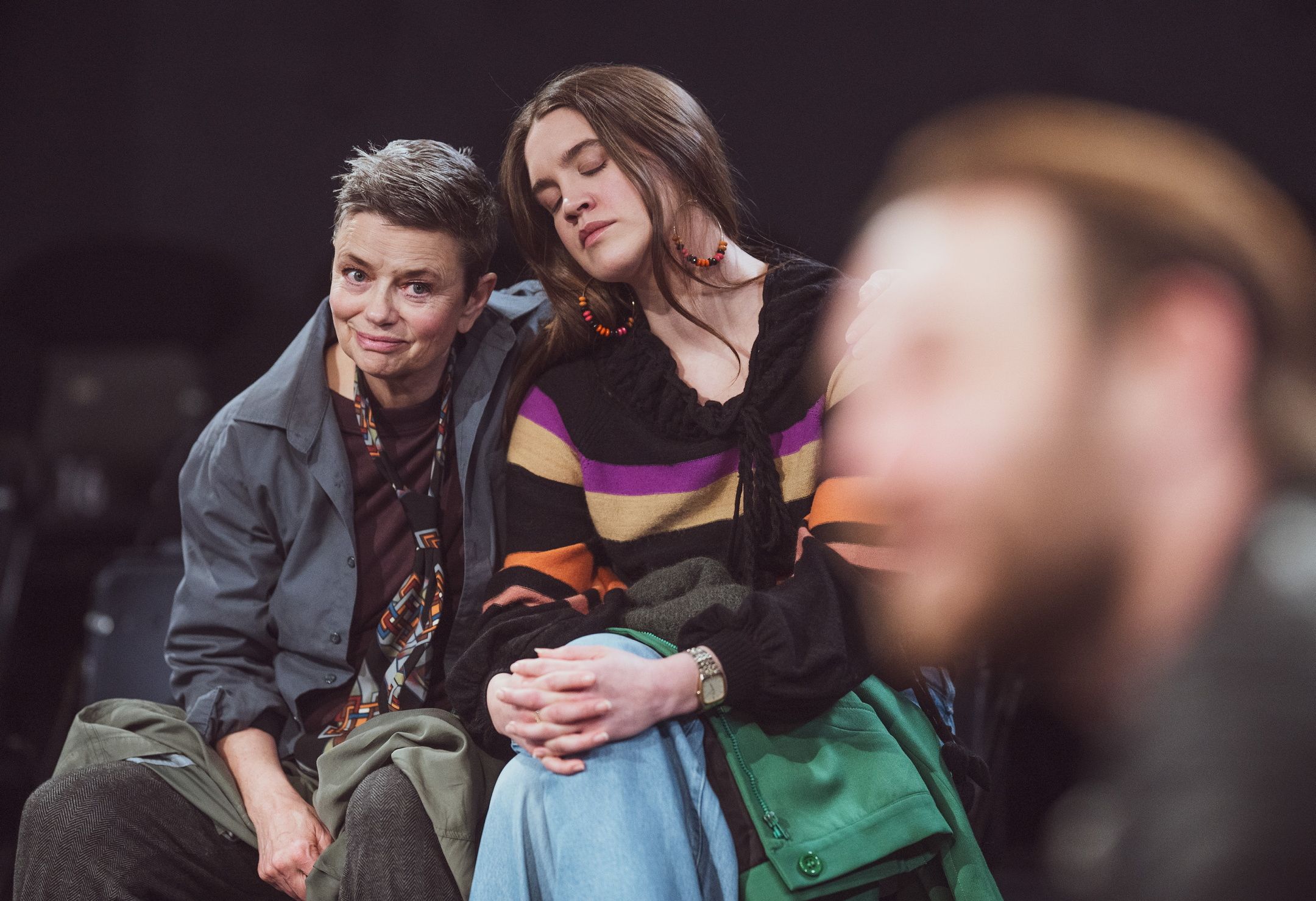 Person med kort hår smiler svakt mens person med langt hår hviler hodet på skulderen hennes