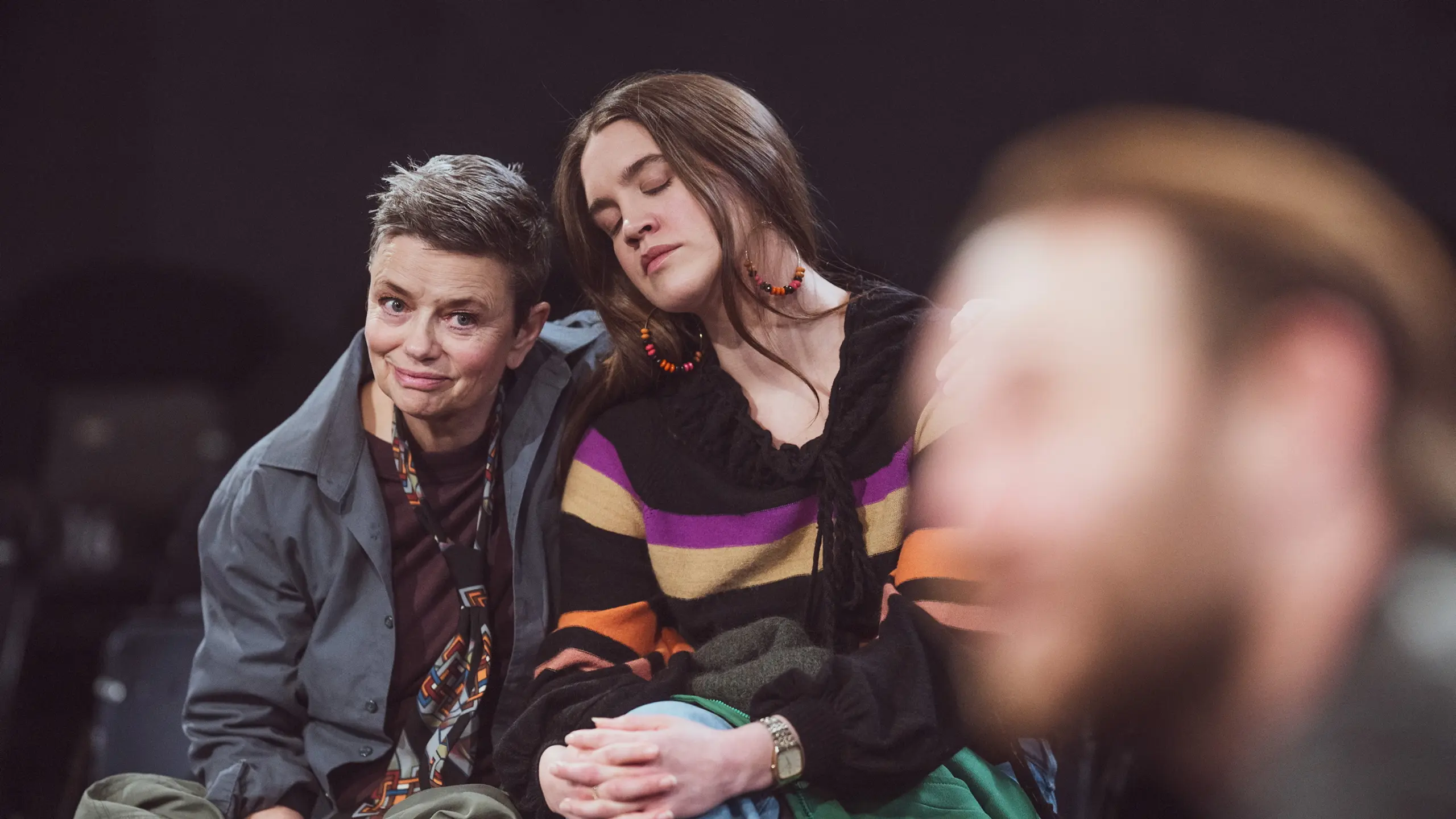 Person med kort hår smiler svakt mens person med langt hår hviler hodet på skulderen hennes