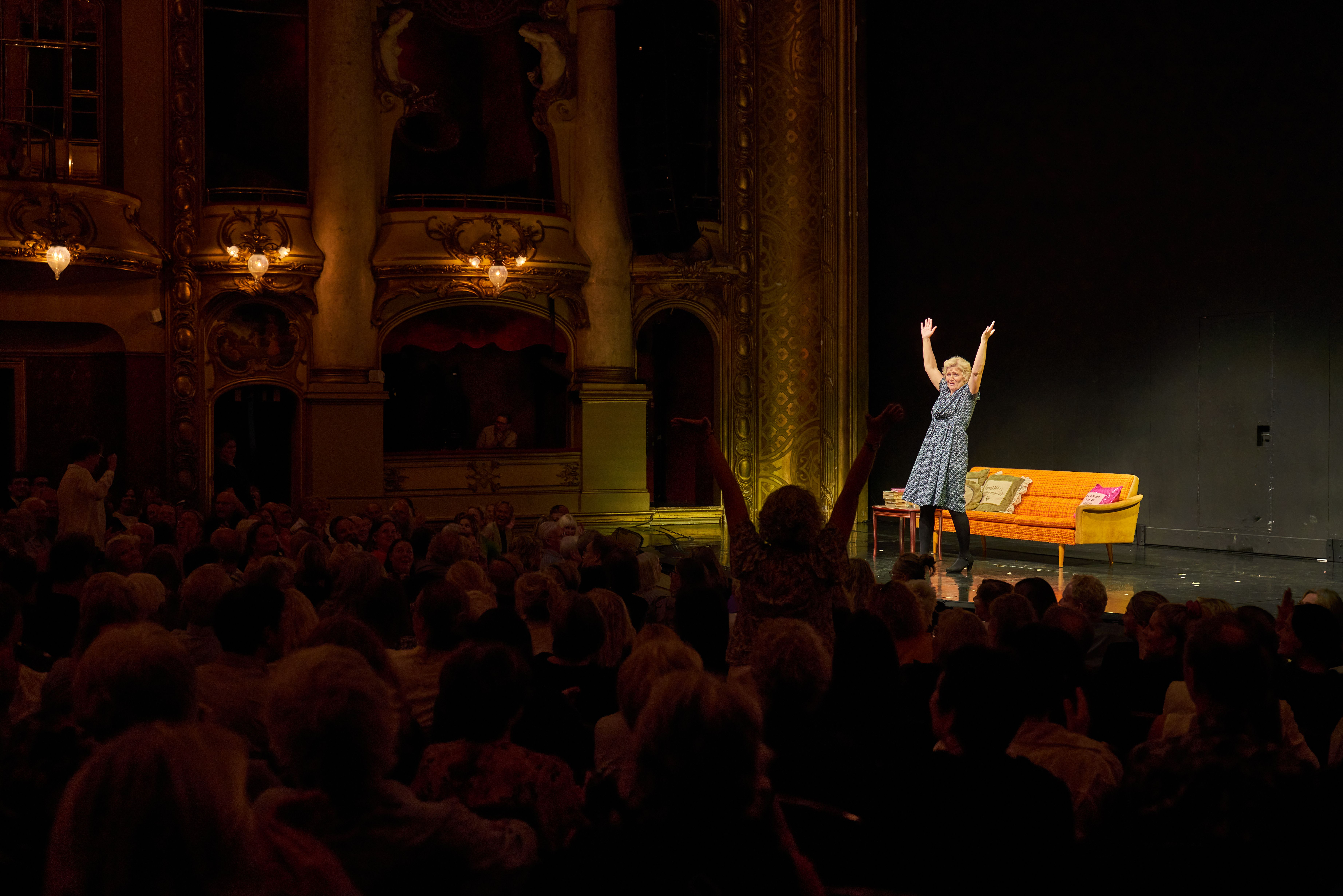 Kvinne står på scene og strekker hendene opp mot publikum. En kvinne i publikum står også oppreist og strekker opp hendene