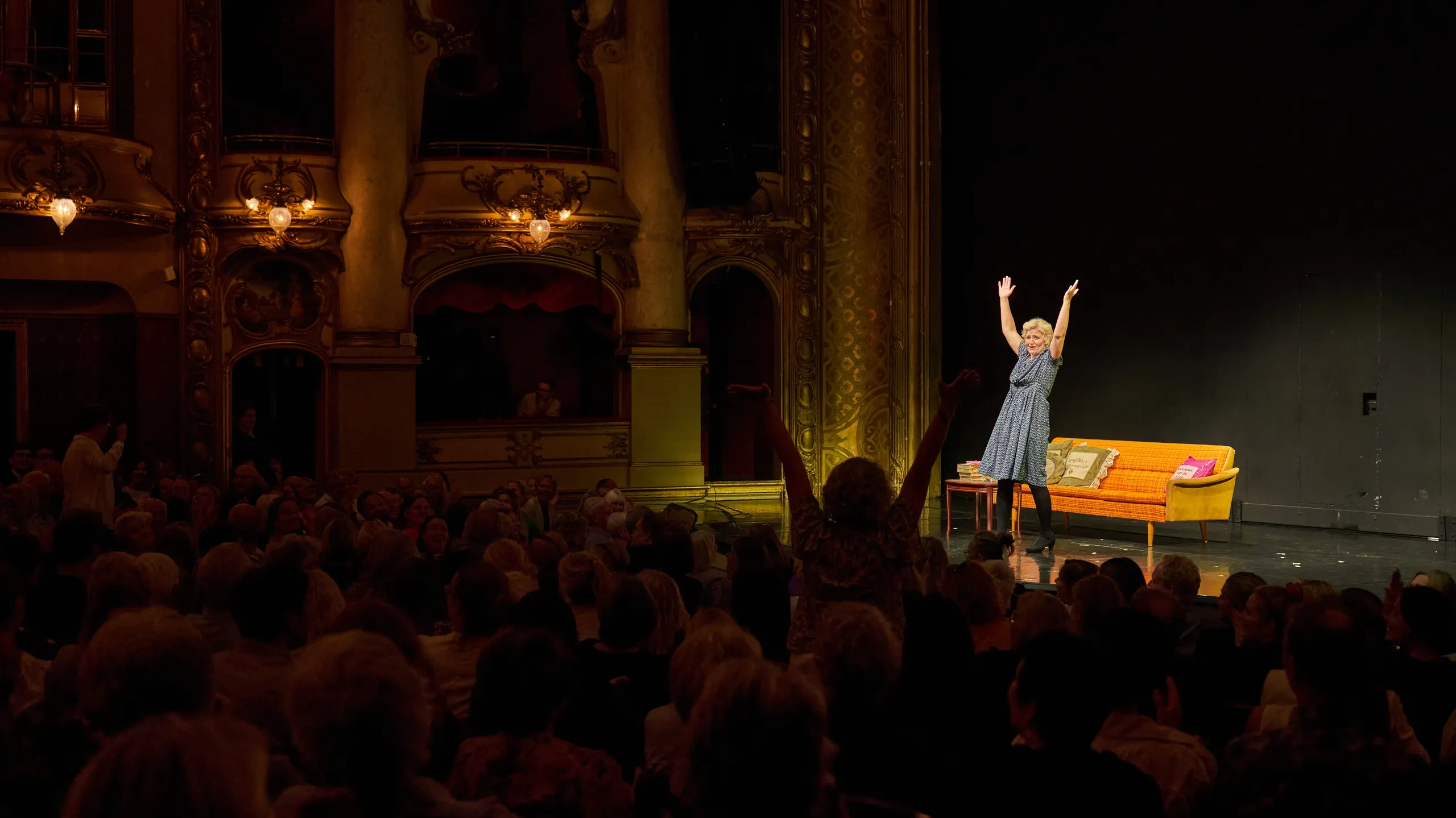Kvinne står på scene og strekker hendene opp mot publikum. En kvinne i publikum står også oppreist og strekker opp hendene