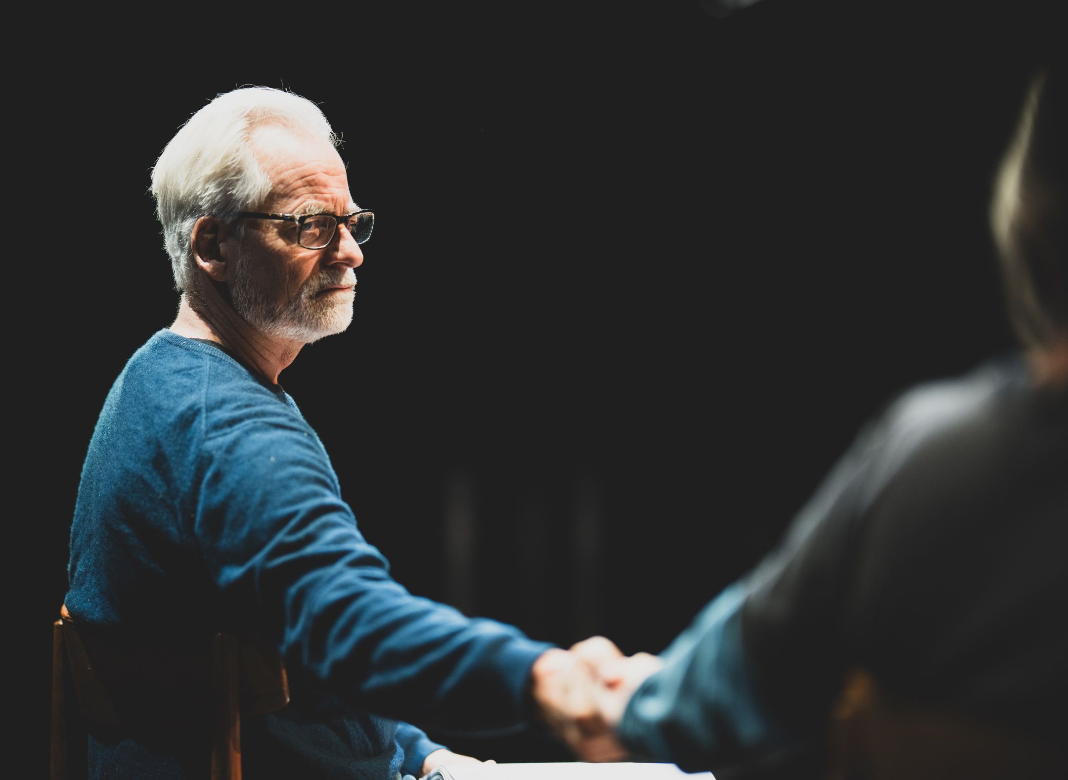 Mann som sitter og ser på en annen person som han holder i hånden