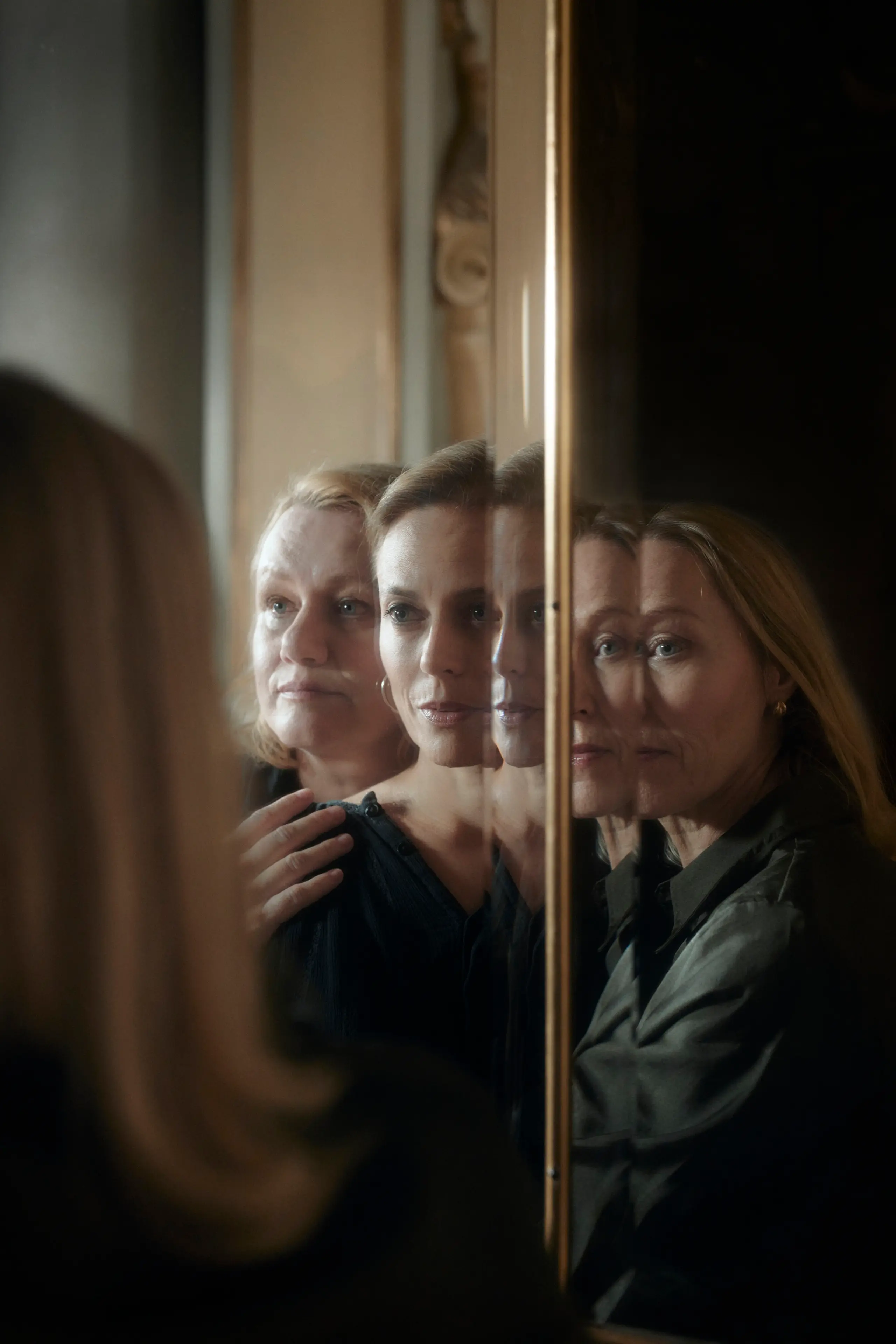 Tre kvinner står foran et speil og holder på hverandre