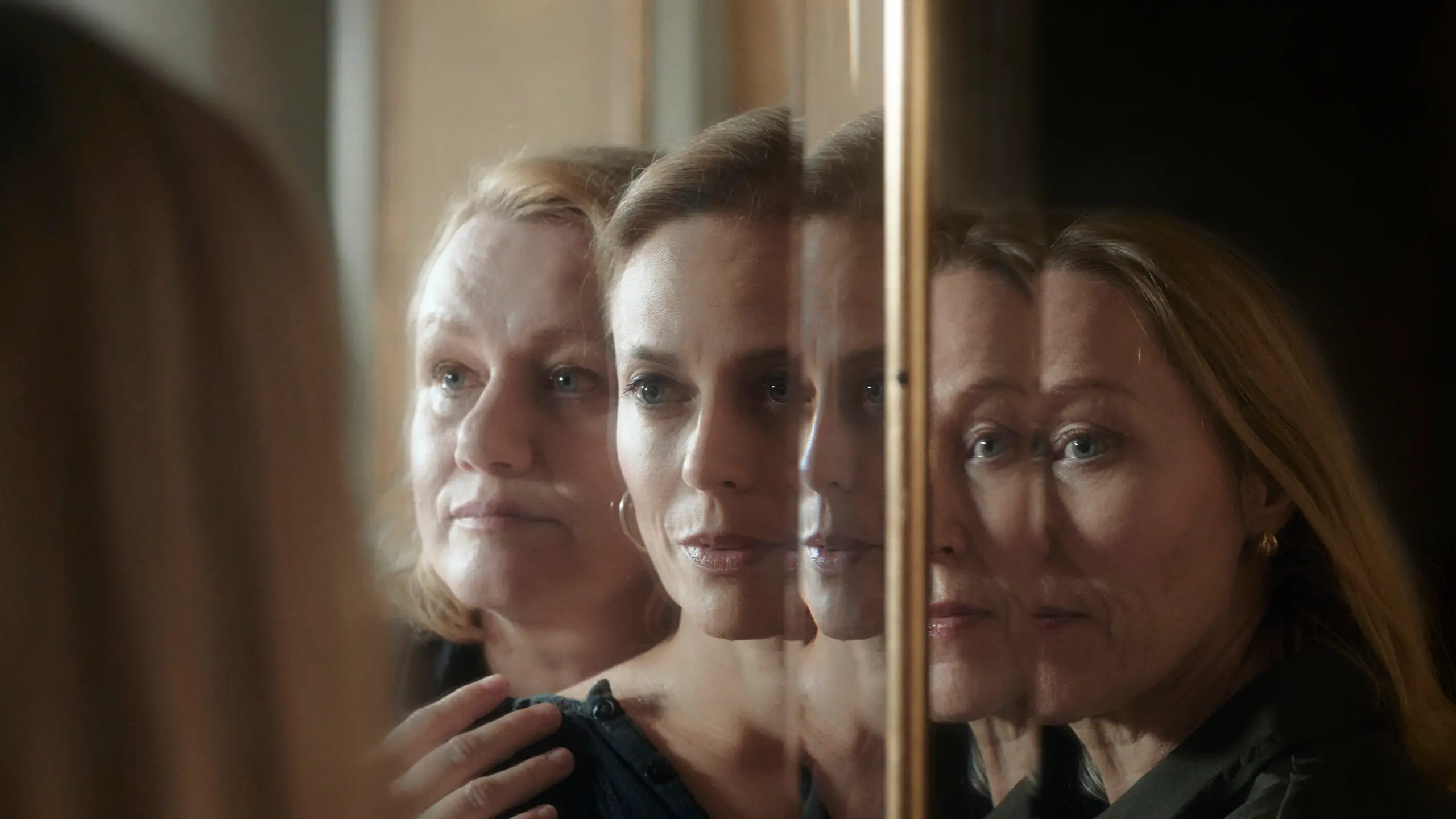 Tre kvinner står foran et speil og holder på hverandre