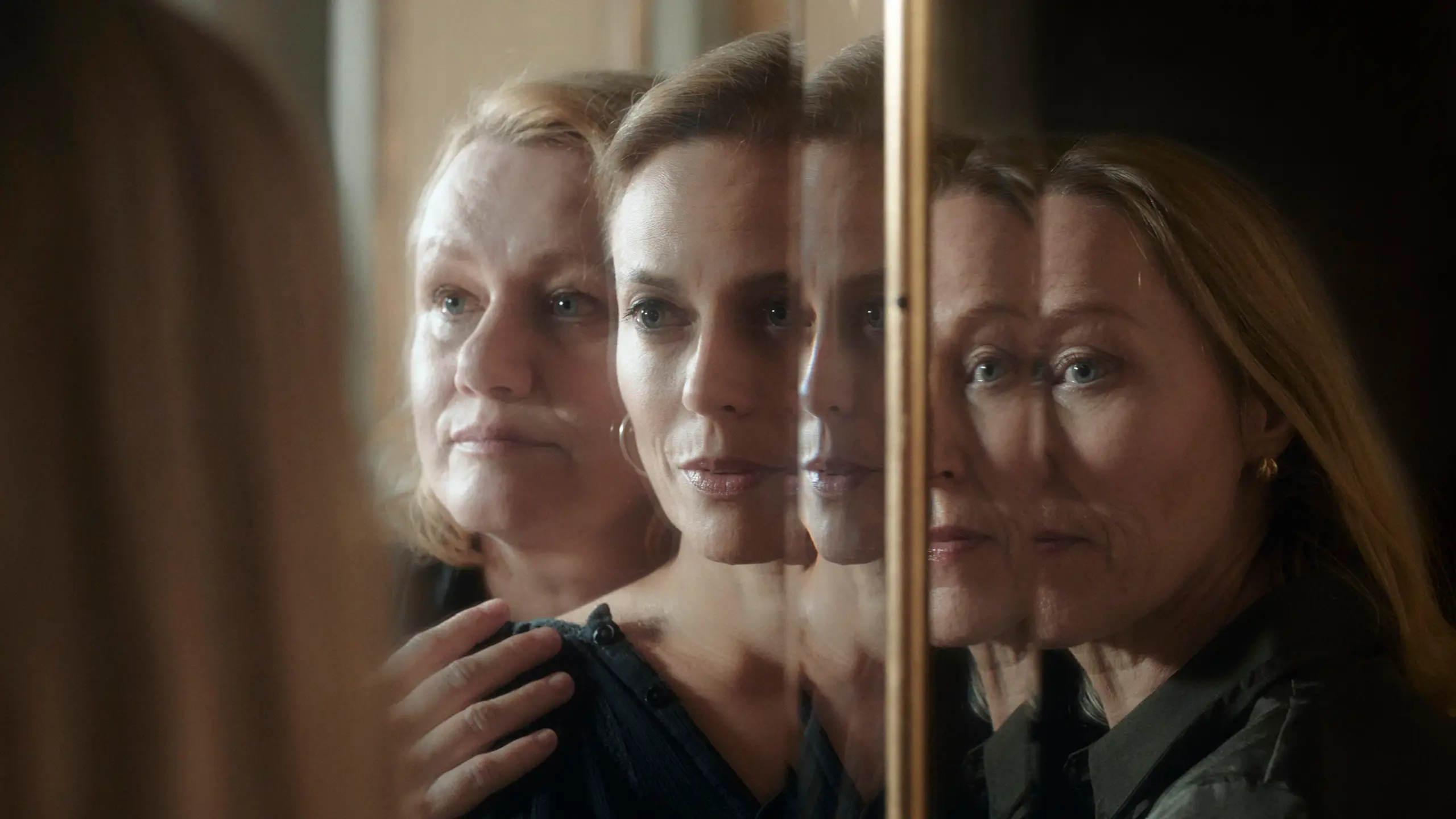 Tre kvinner står foran et speil og holder på hverandre