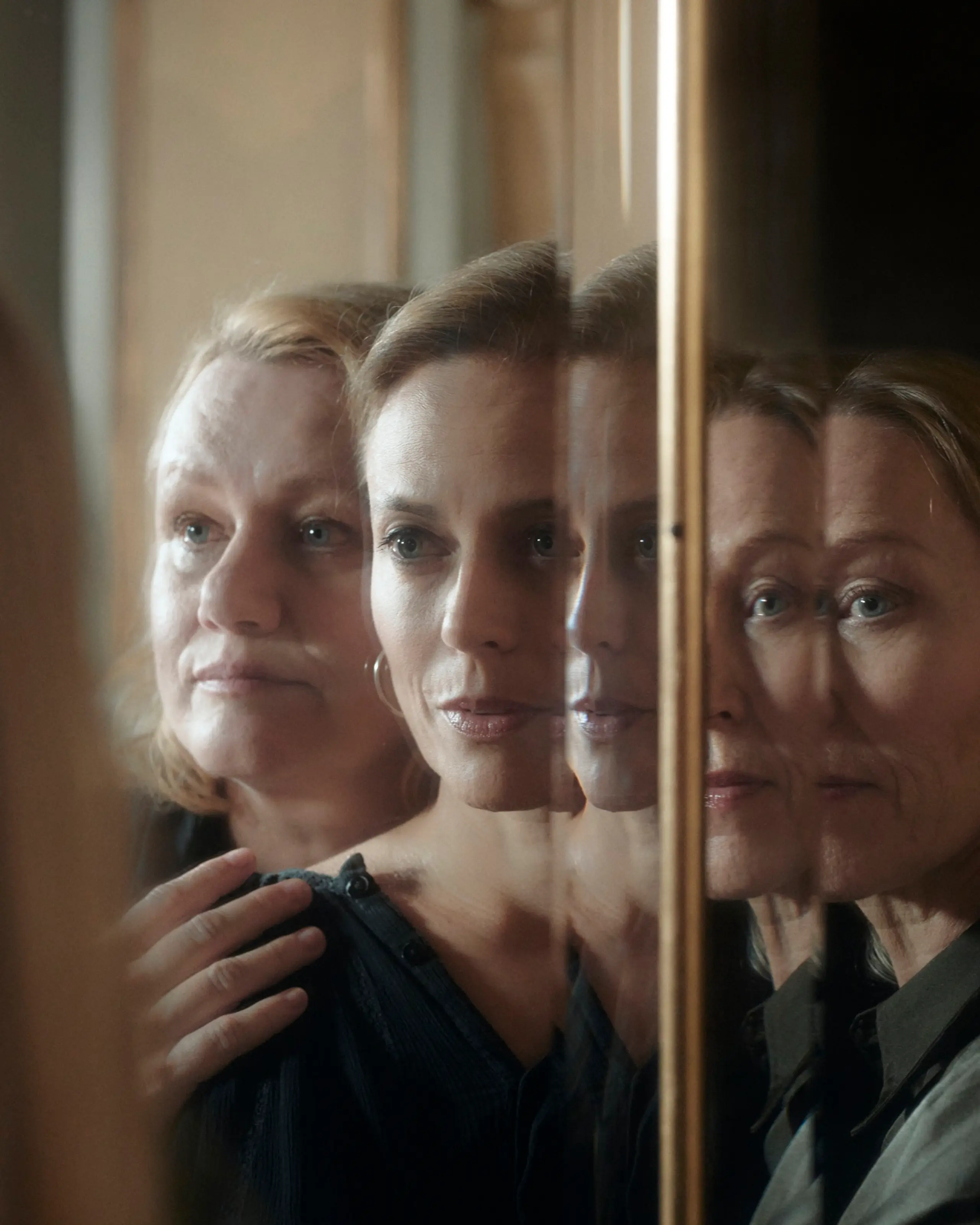 Tre kvinner står foran et speil og holder på hverandre