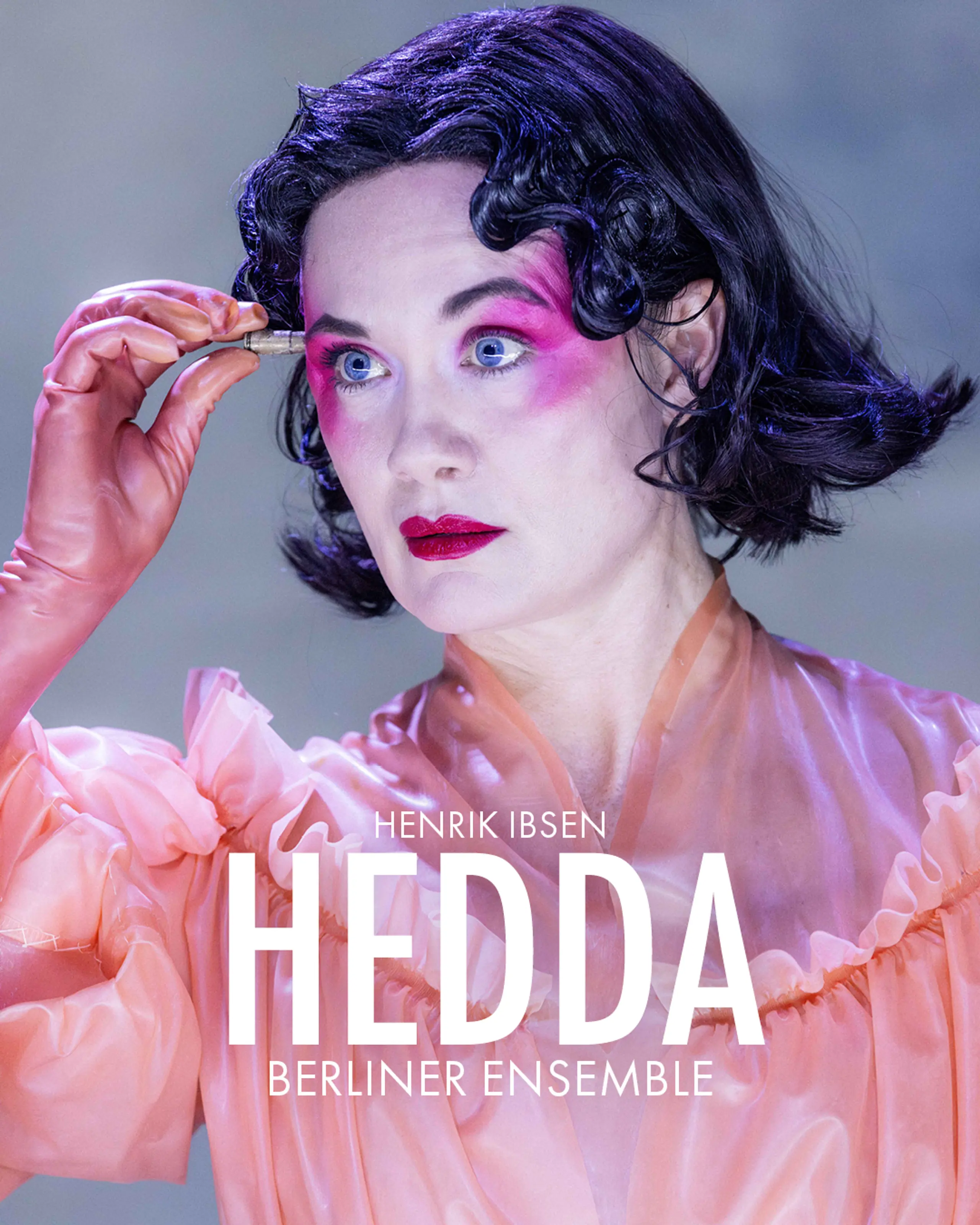 Person med kort mørkt hår, kraftig rosa øyenskygge og ferskenfarget kjole holder en liten patron foran pannen. Med tekst "Henrik Ibsens Hedda Berliner Ensemble