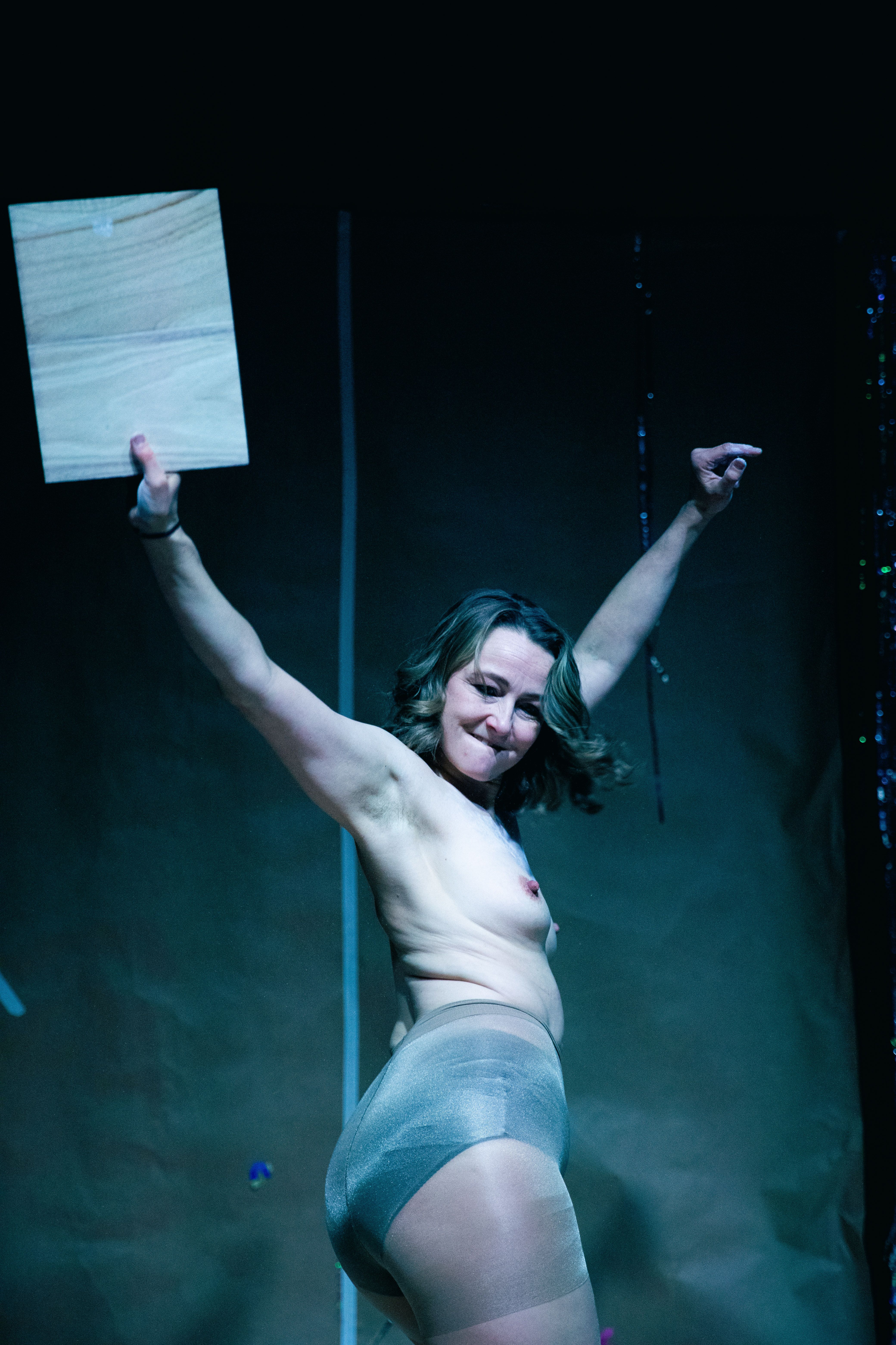 Kvinne i bar overkropp og strømpebukser står med armene seirende opp