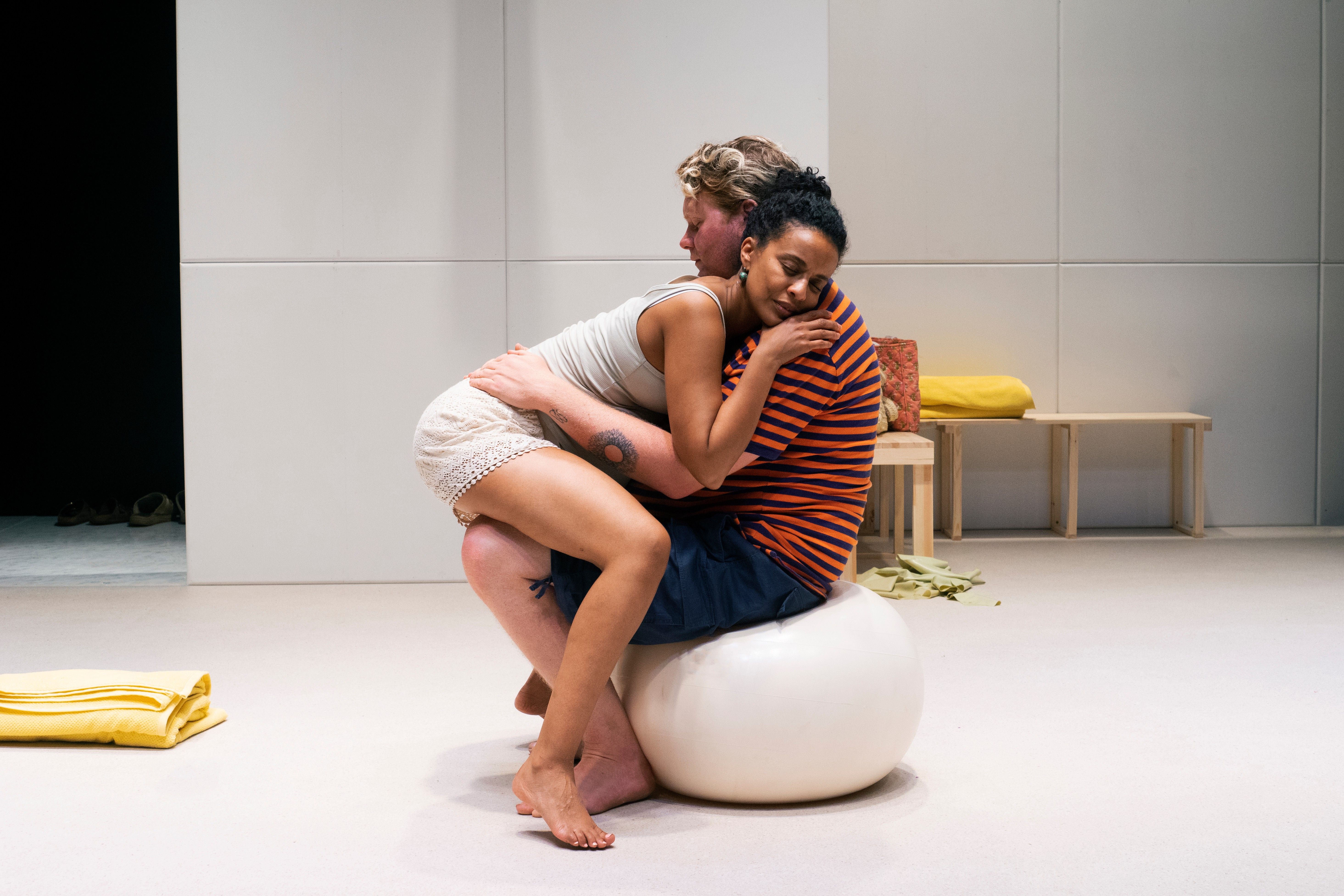 Et gravid par sitter tett sammen på en pilatesball, kvinnen med øynene lukket og hodet hvilende på mannens skulder.