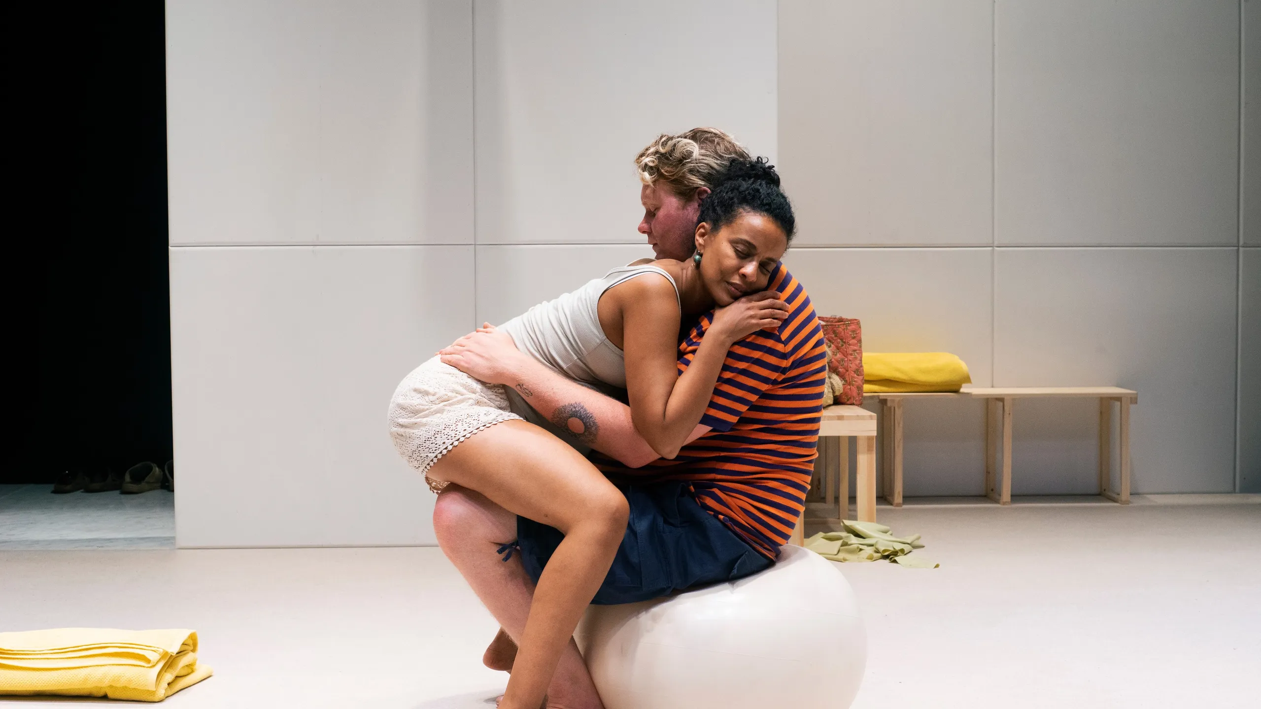 Et gravid par sitter tett sammen på en pilatesball, kvinnen med øynene lukket og hodet hvilende på mannens skulder.