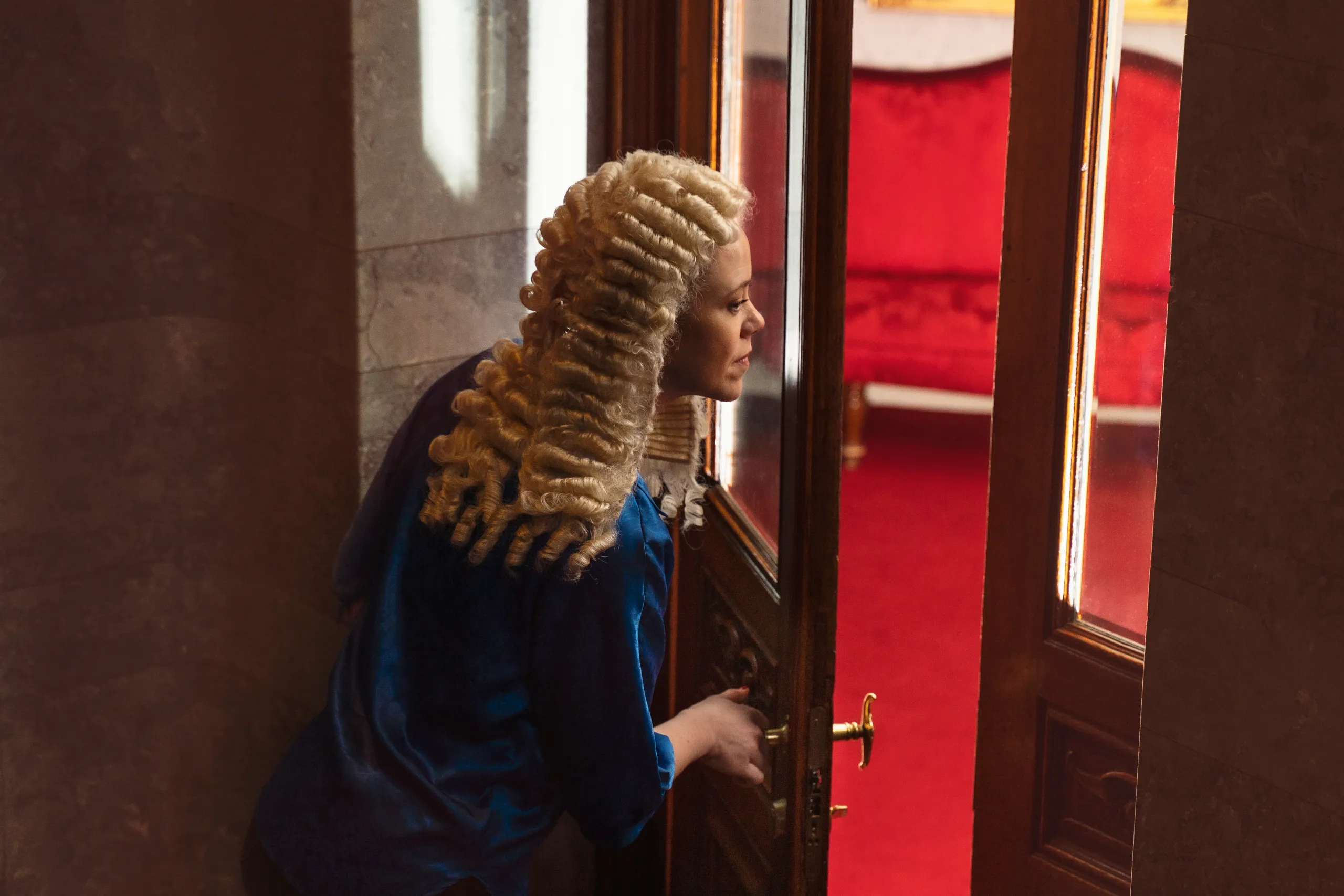 Person med Holberg-parykk ser gjennom døråpning