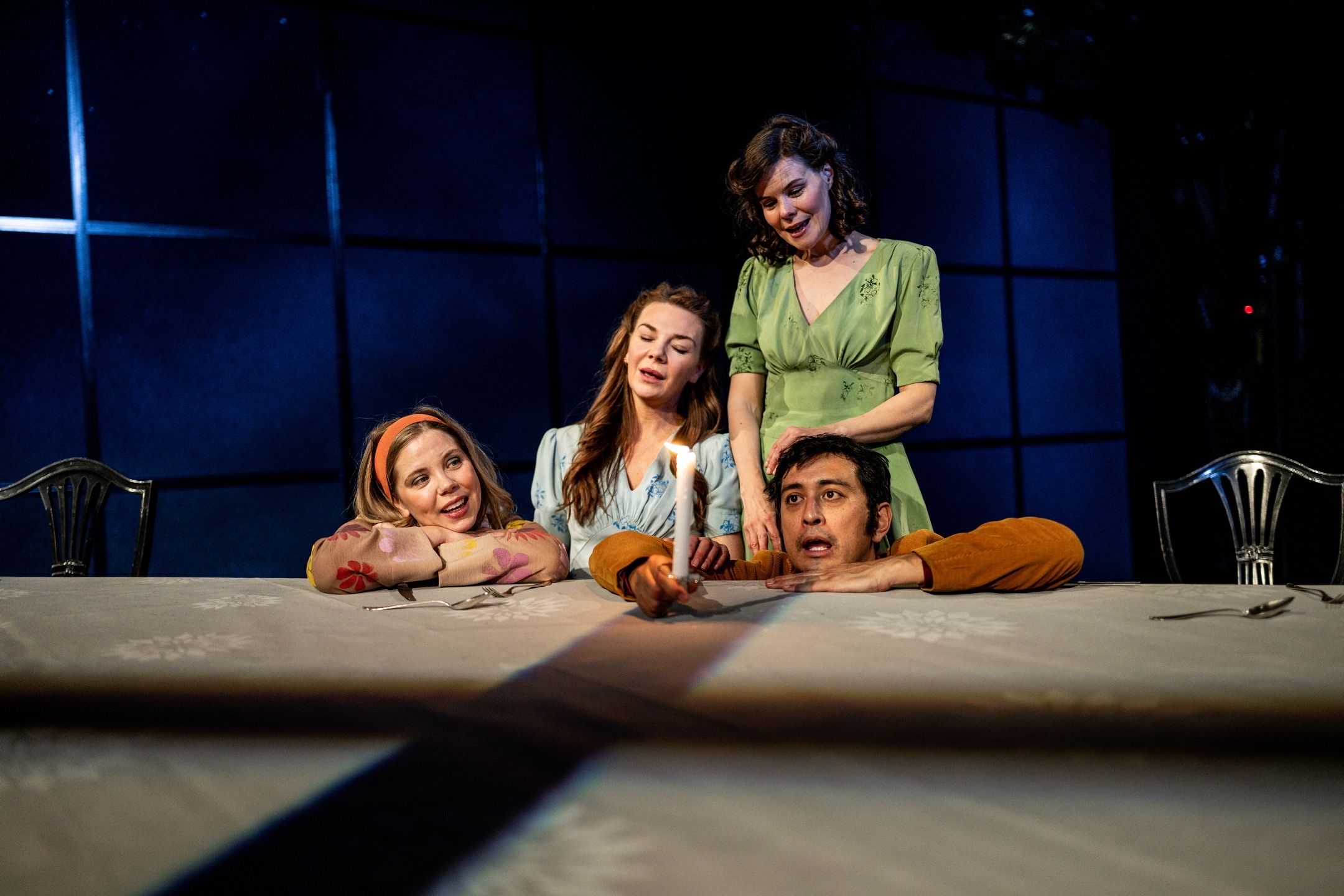 Fire personer rundt bordet med levende lys; én kvinne støtter hodet på armene og smiler.