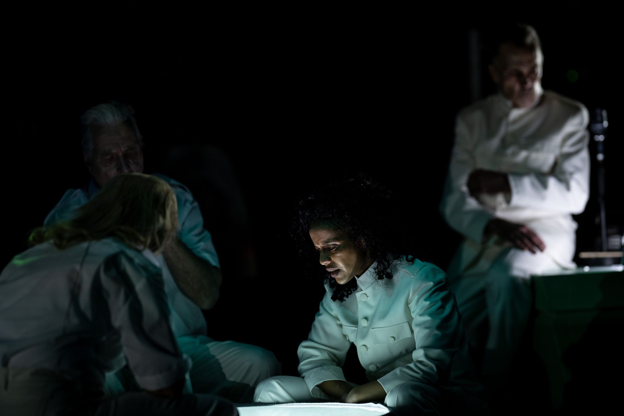 Skuespillere på en mørk scene i lyse kostymer