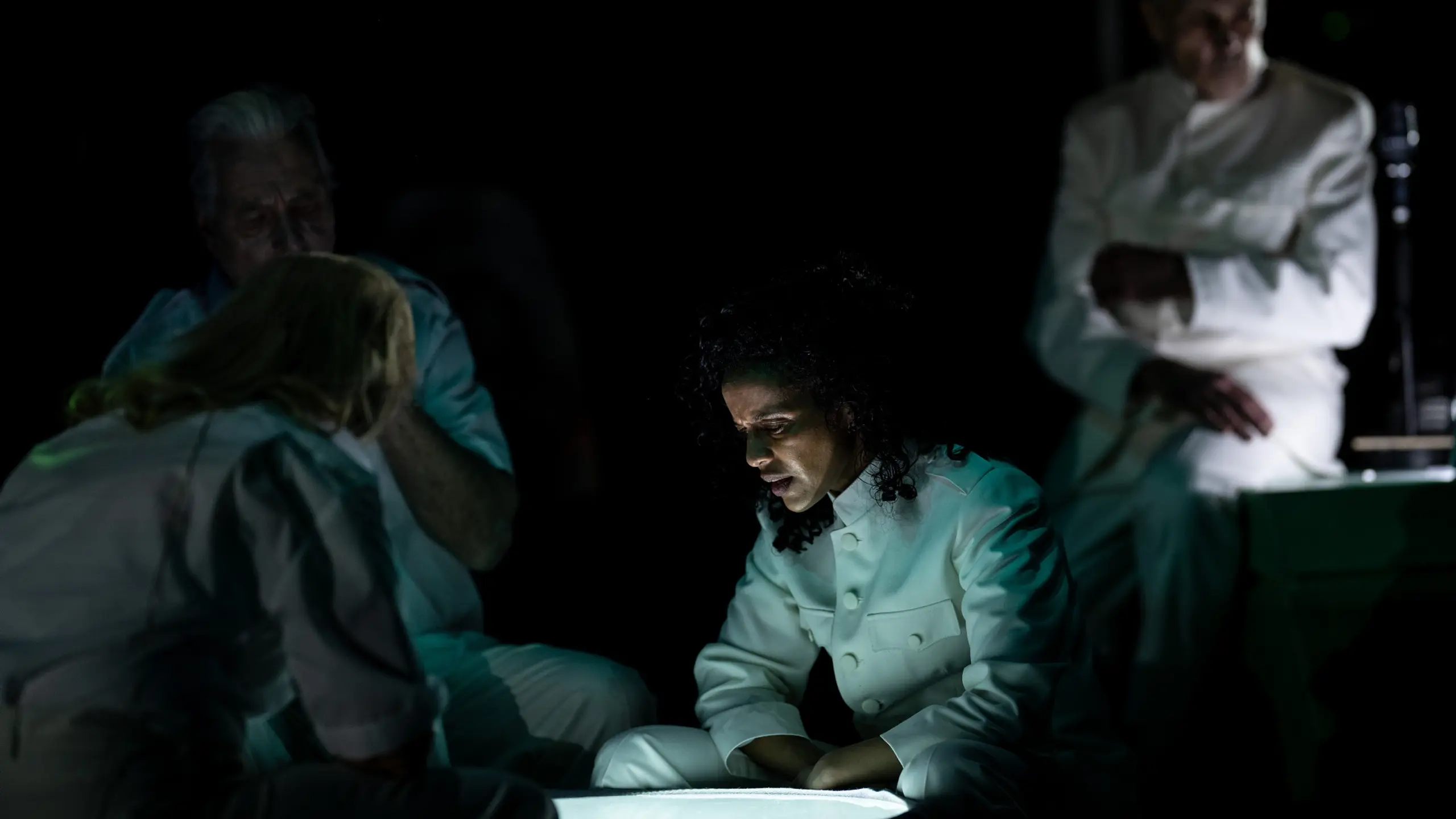 Skuespillere på en mørk scene i lyse kostymer