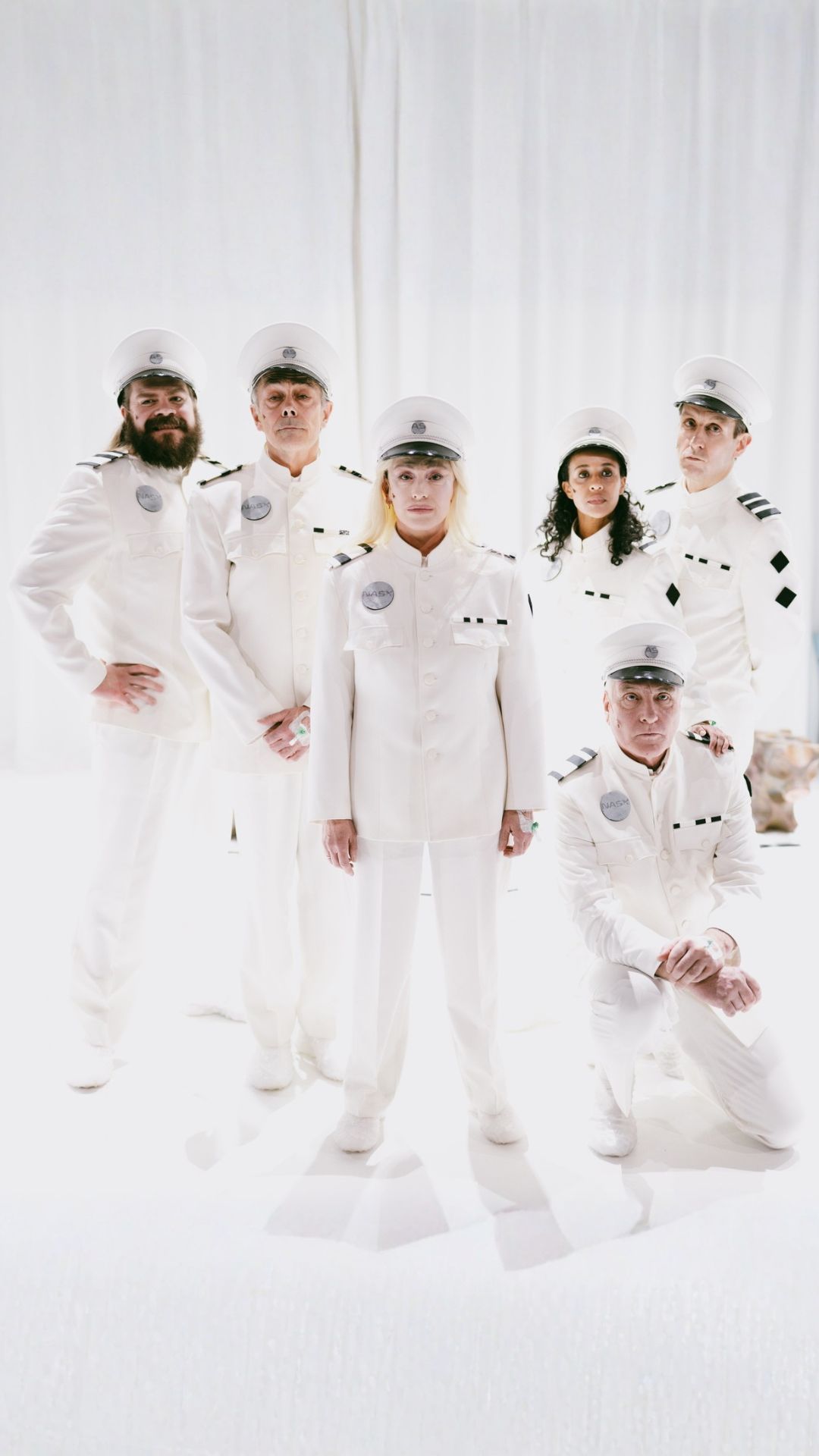 Seks personer i hvite futuristiske kostymer stilt opp til gruppebilde