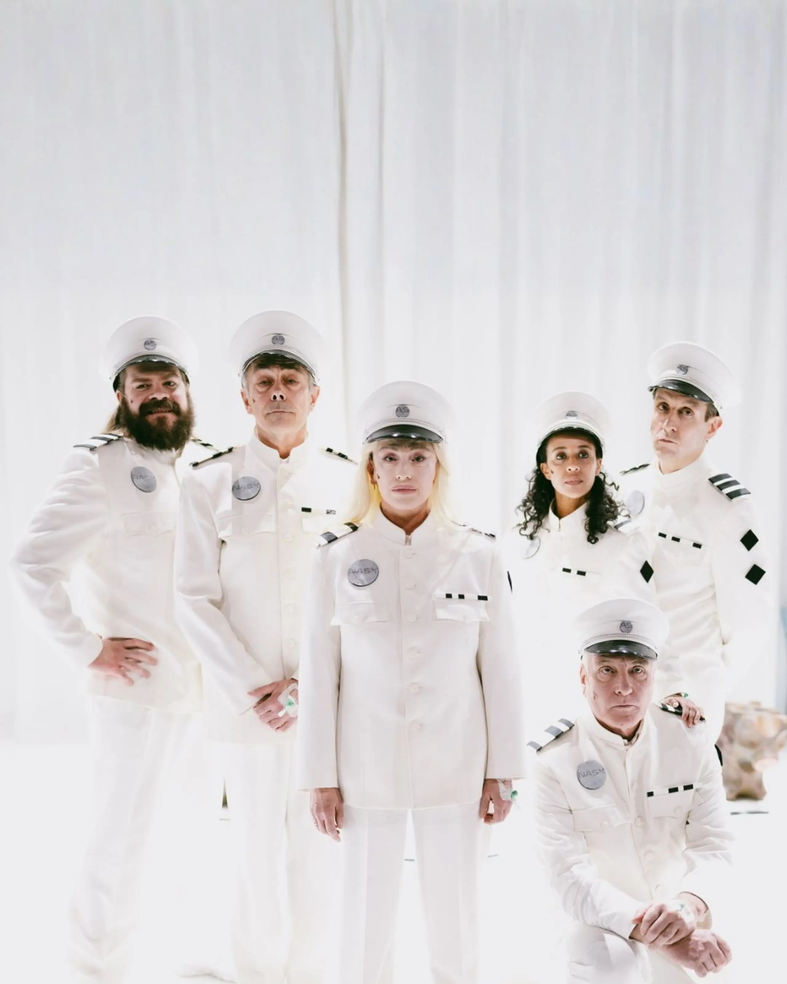 Seks personer i hvite futuristiske kostymer stilt opp til gruppebilde