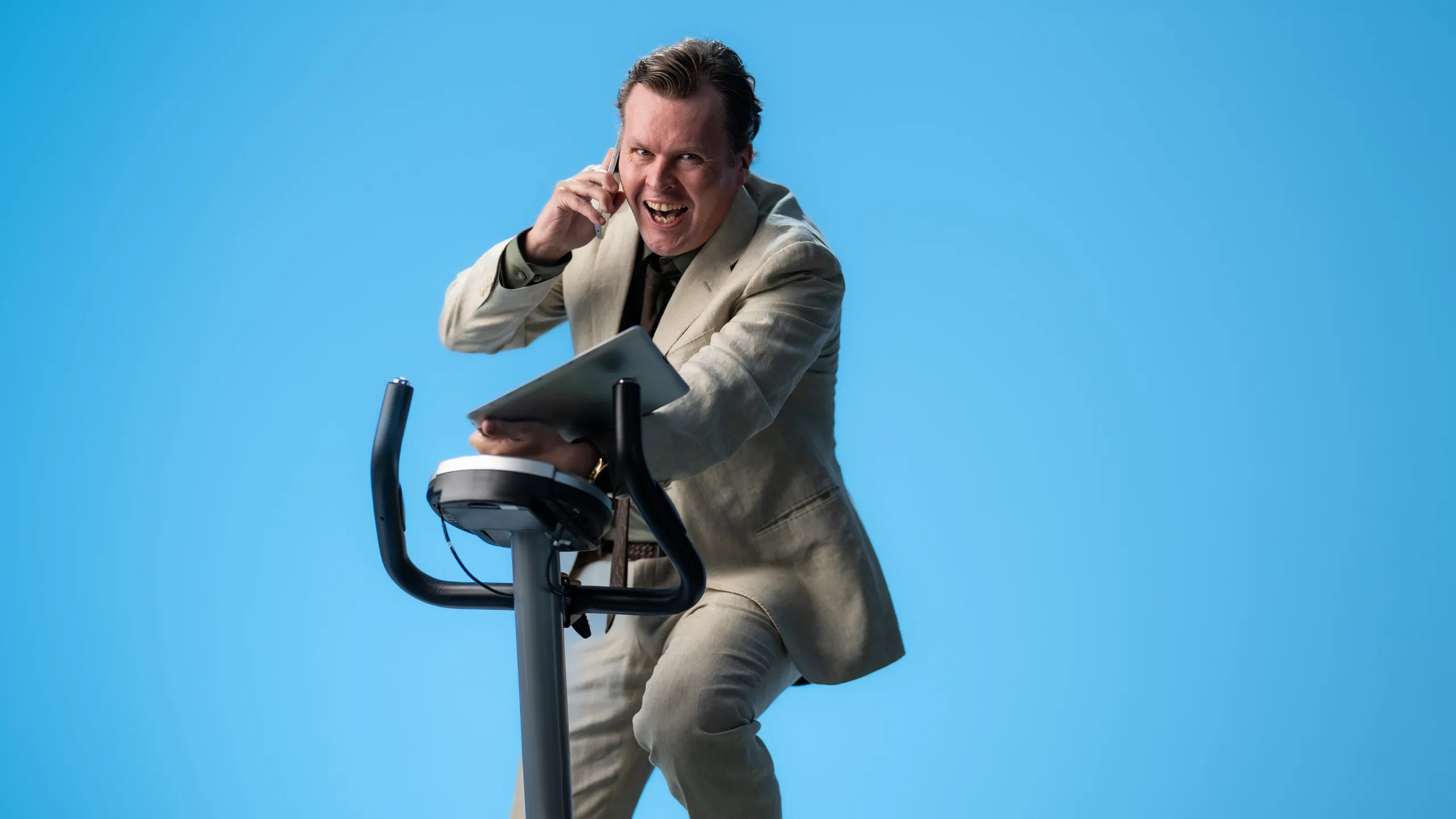 Smilende mann i dress som snakker i telefonen på ergometersykkel.