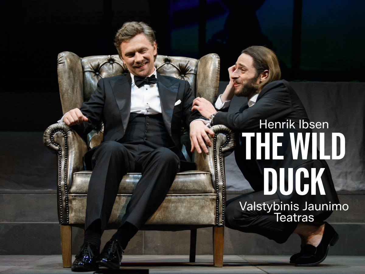 Smilende mann i smoking sitter i en skinnlenestol mens en annen mann på huk lener seg mot armlenet under en samtale. Med tittel "Henrik Ibsen The Wild Duck"