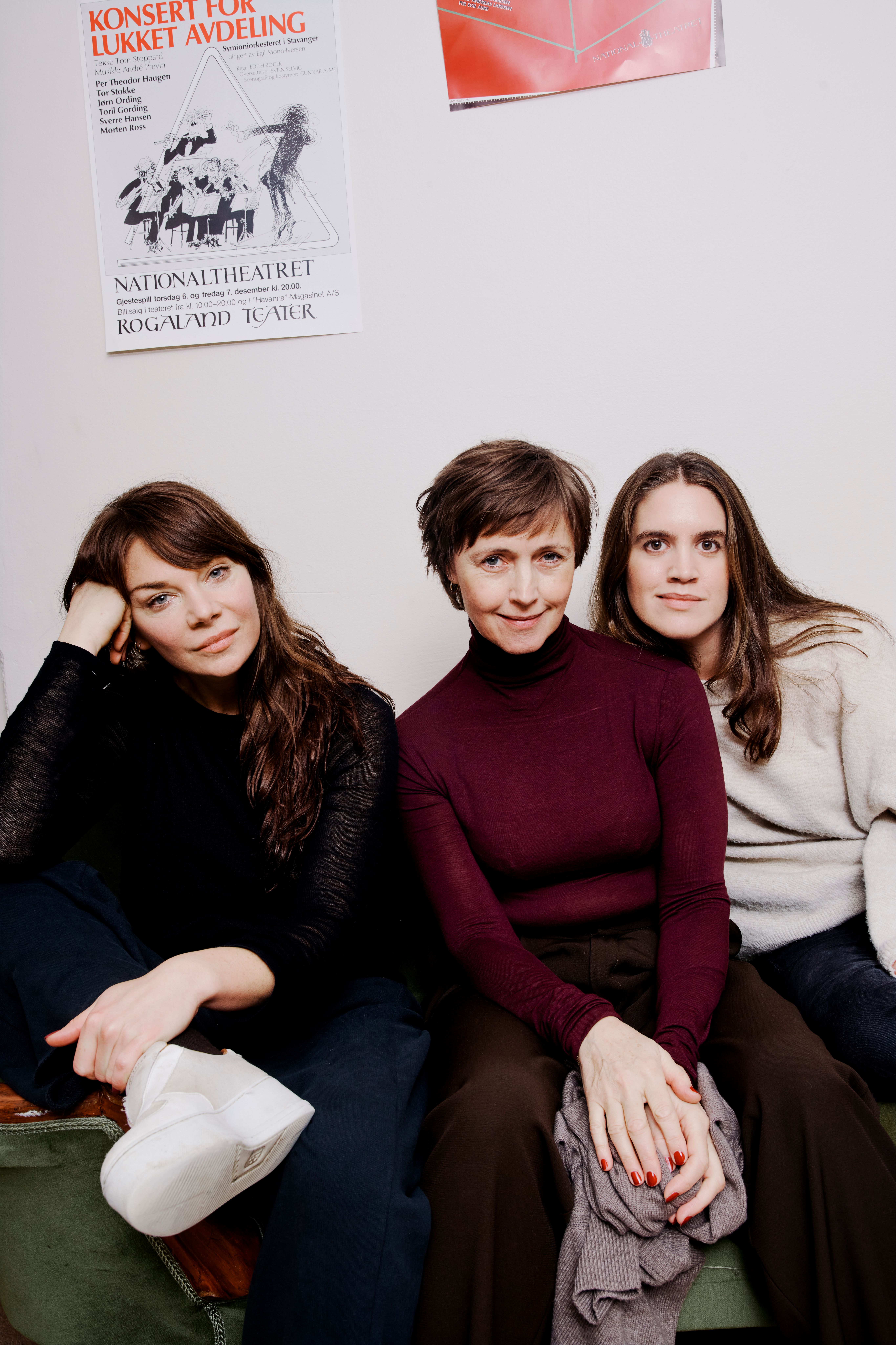 Tre kvinner sitter i en grønn sofa mot en hvit vegg.