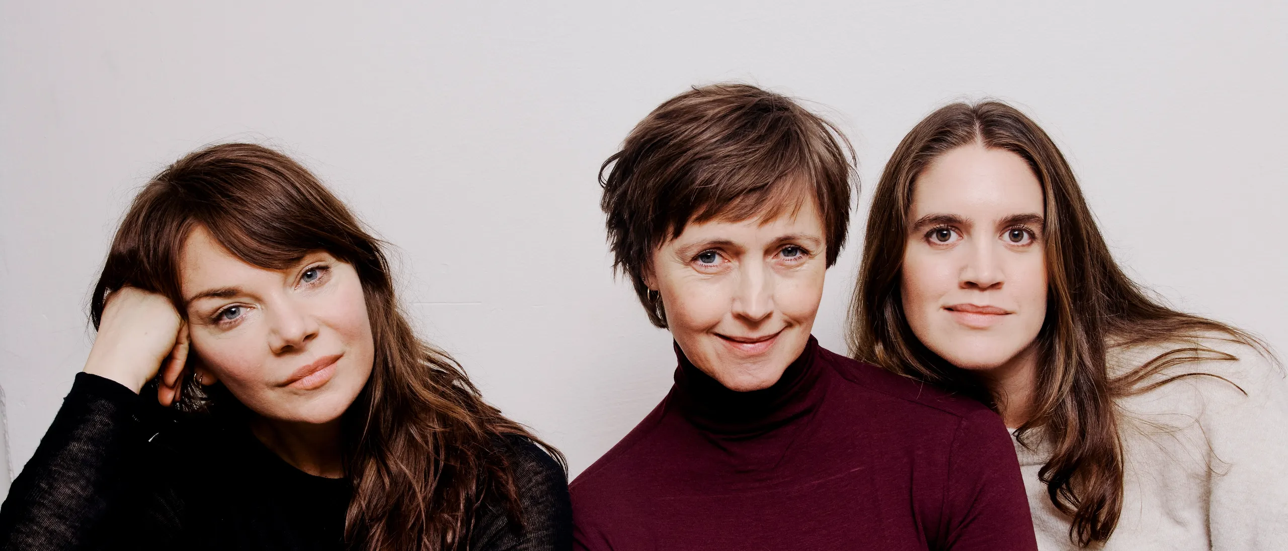 Tre kvinner sitter i en grønn sofa mot en hvit vegg.