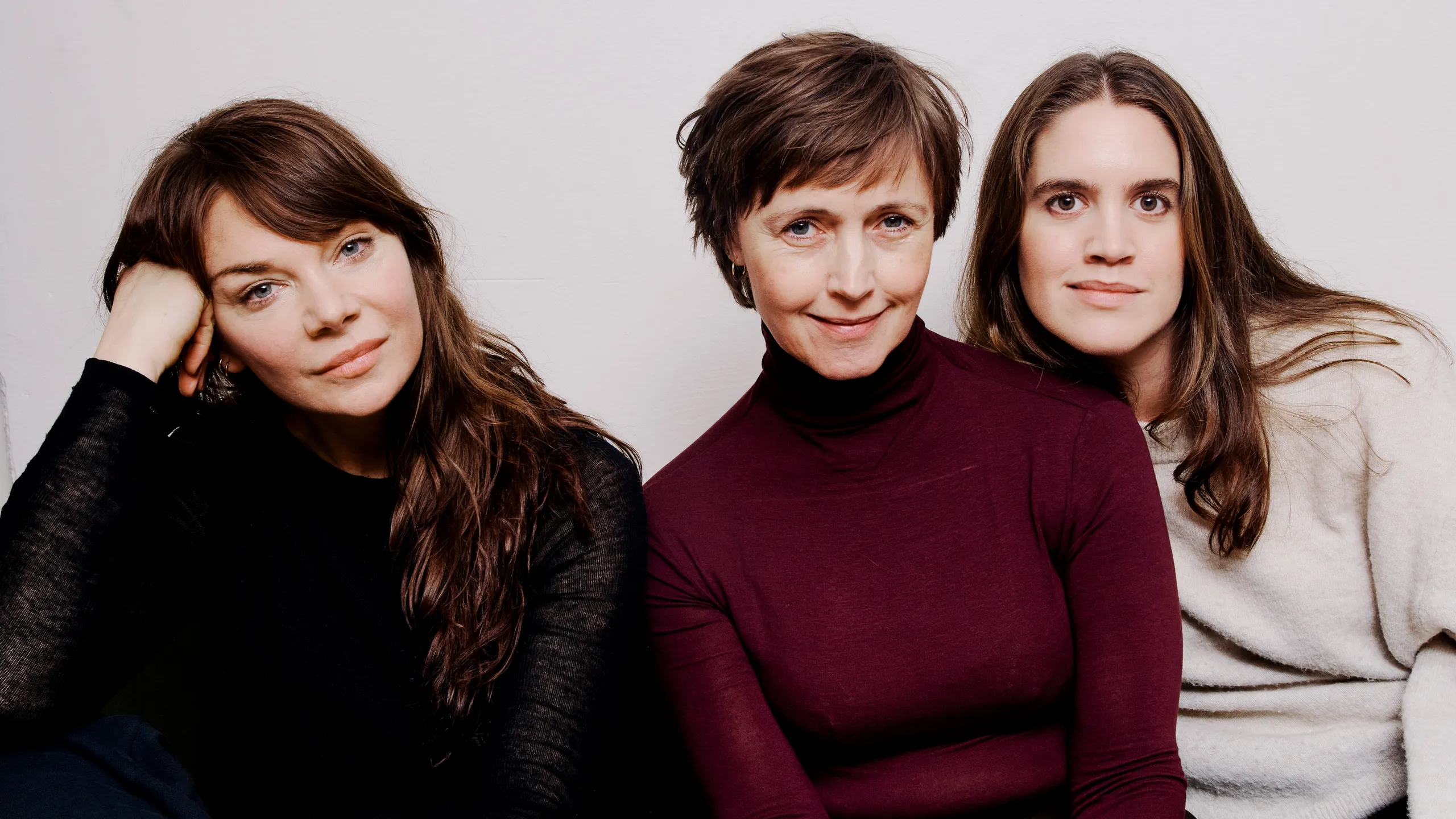 Tre kvinner sitter i en grønn sofa mot en hvit vegg.