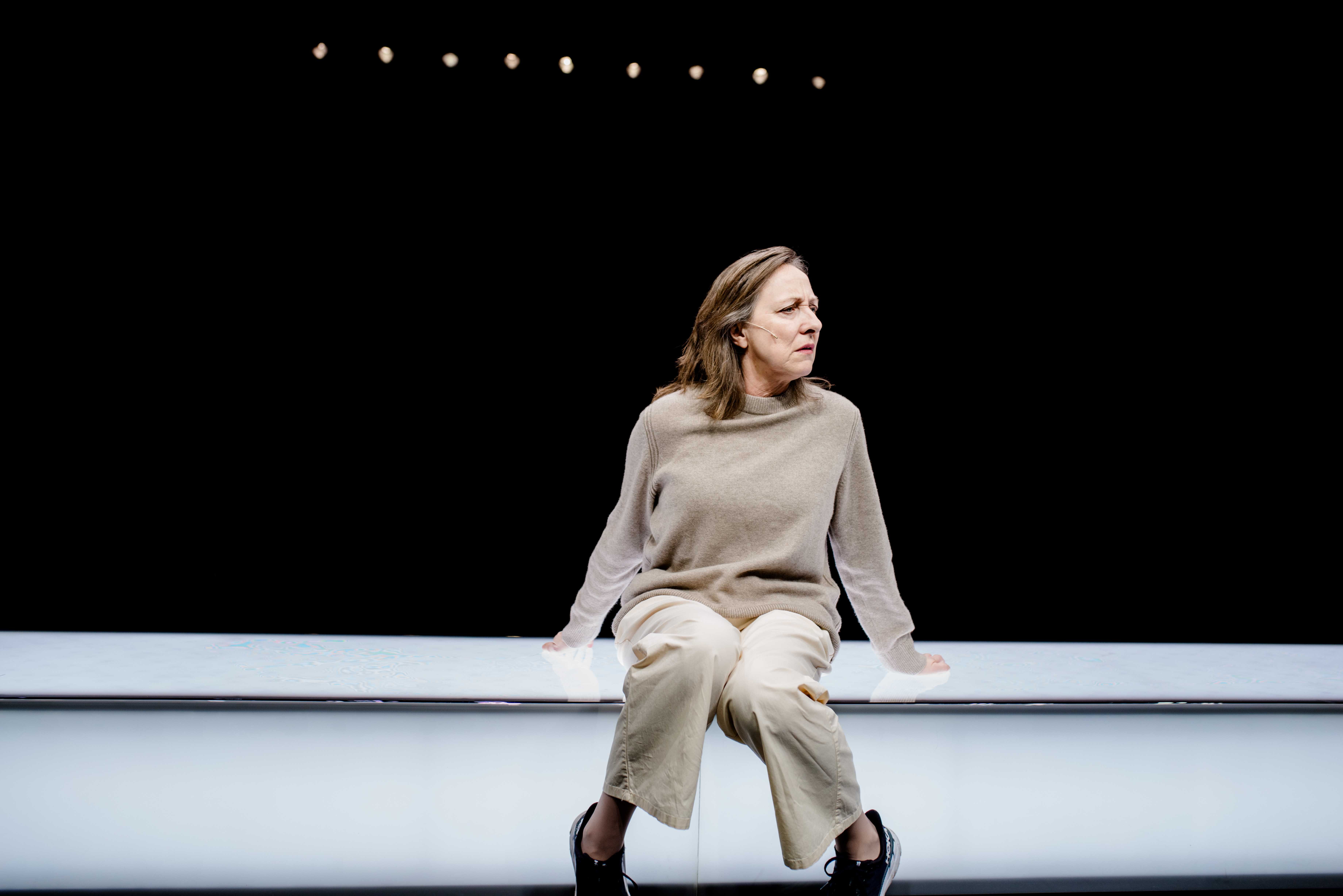 Kvinne sitter på lang hvit benk og ser bekymret ut