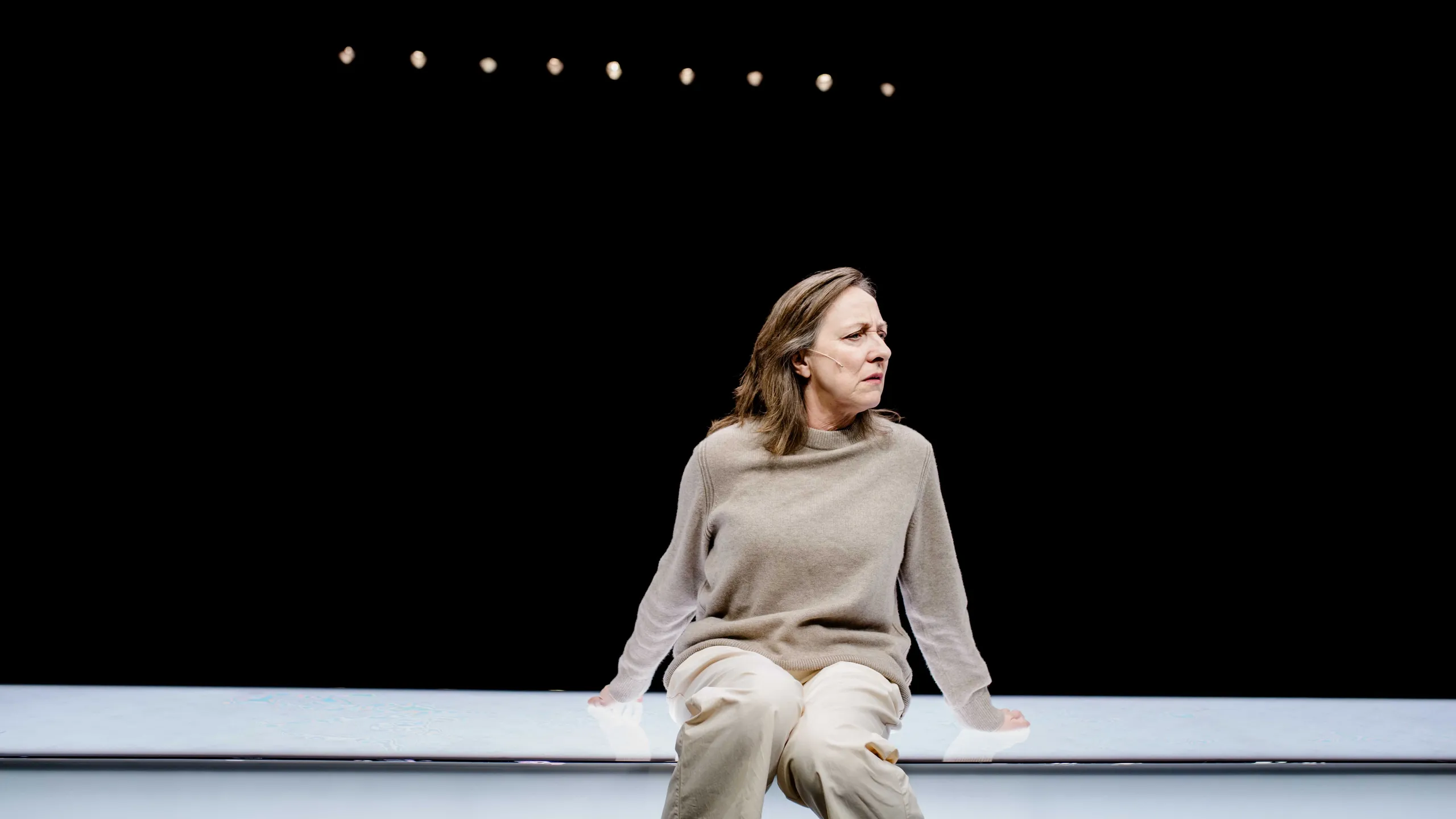 Kvinne sitter på lang hvit benk og ser bekymret ut