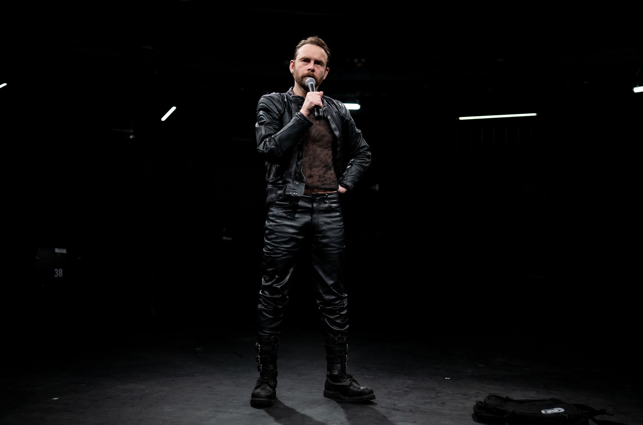 Mann i skinnklær står og prater i mikrofon