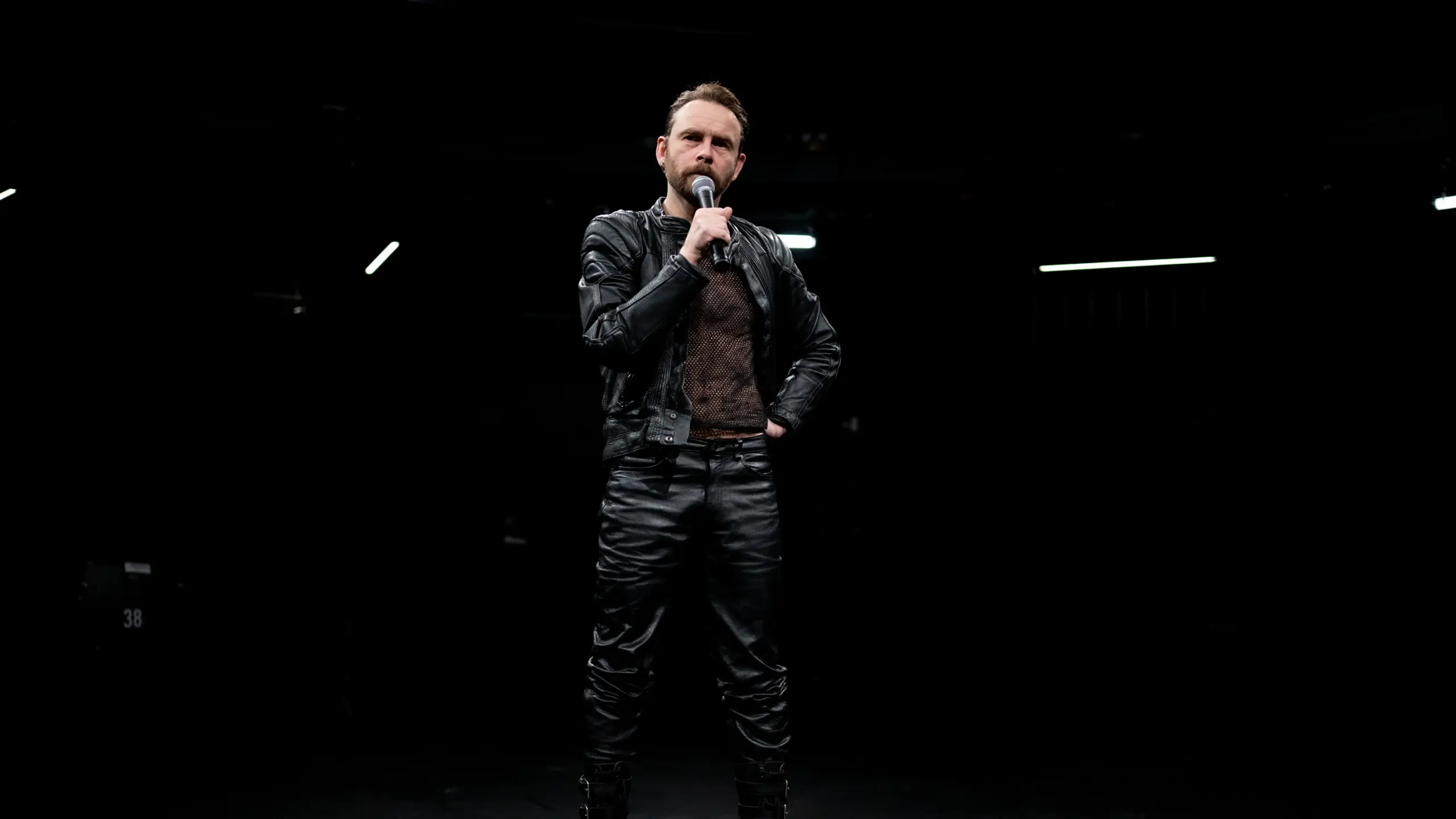 Mann i skinnklær står og prater i mikrofon