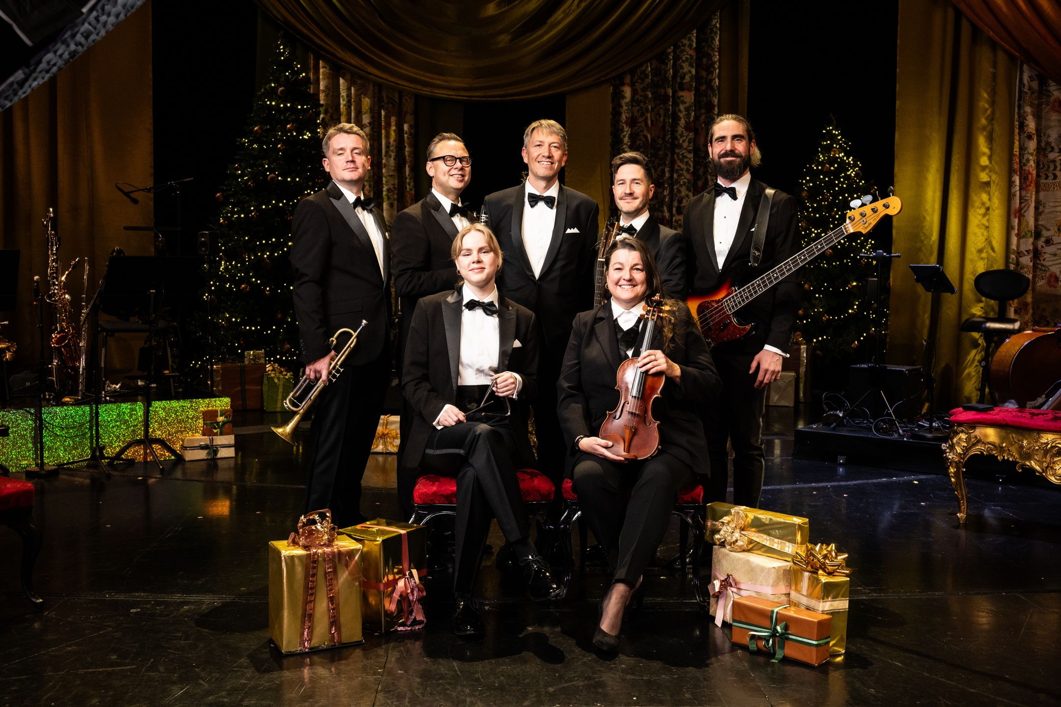 Gruppebilde av syv musikere på julepyntet scene