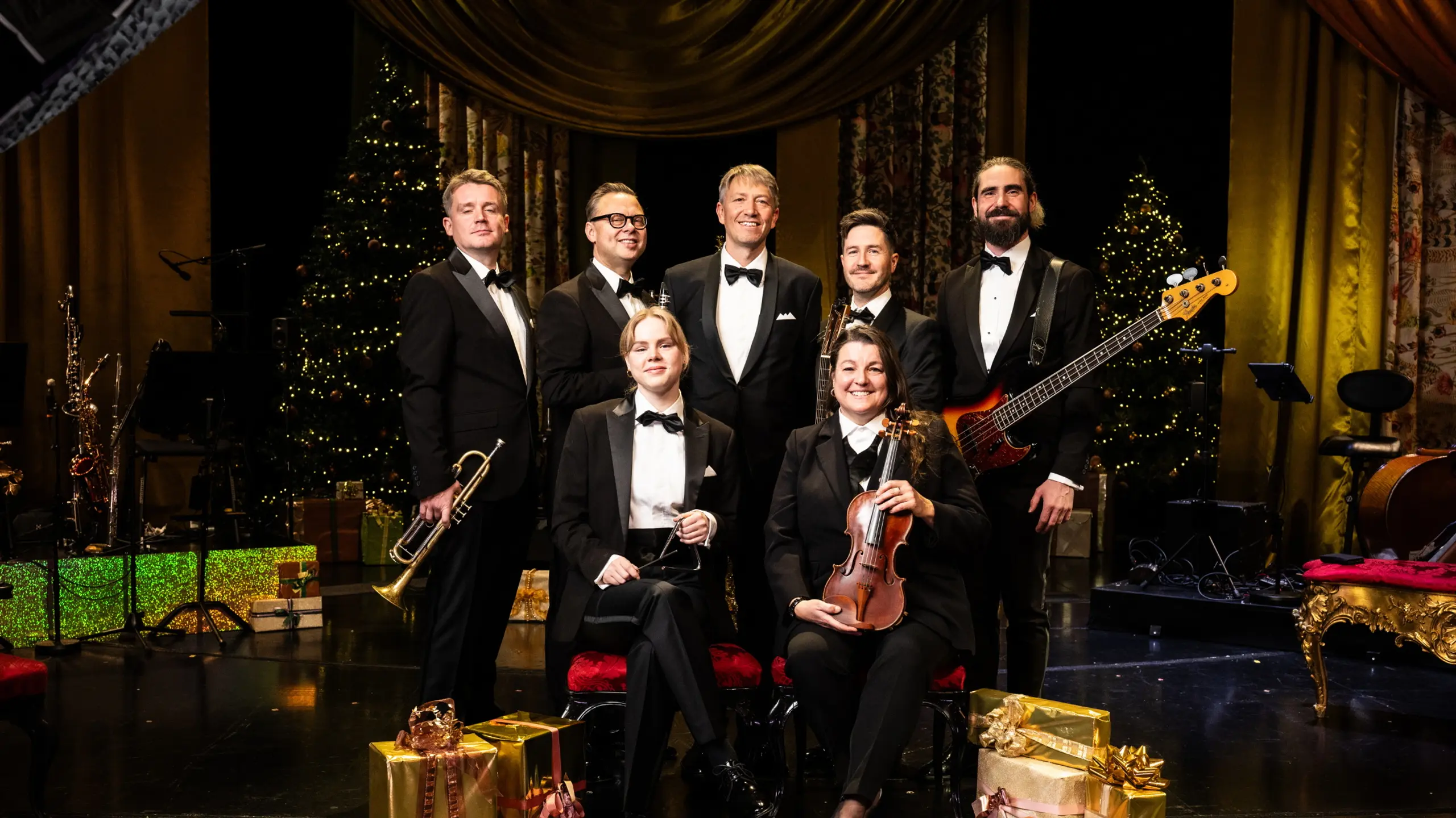 Gruppebilde av syv musikere på julepyntet scene