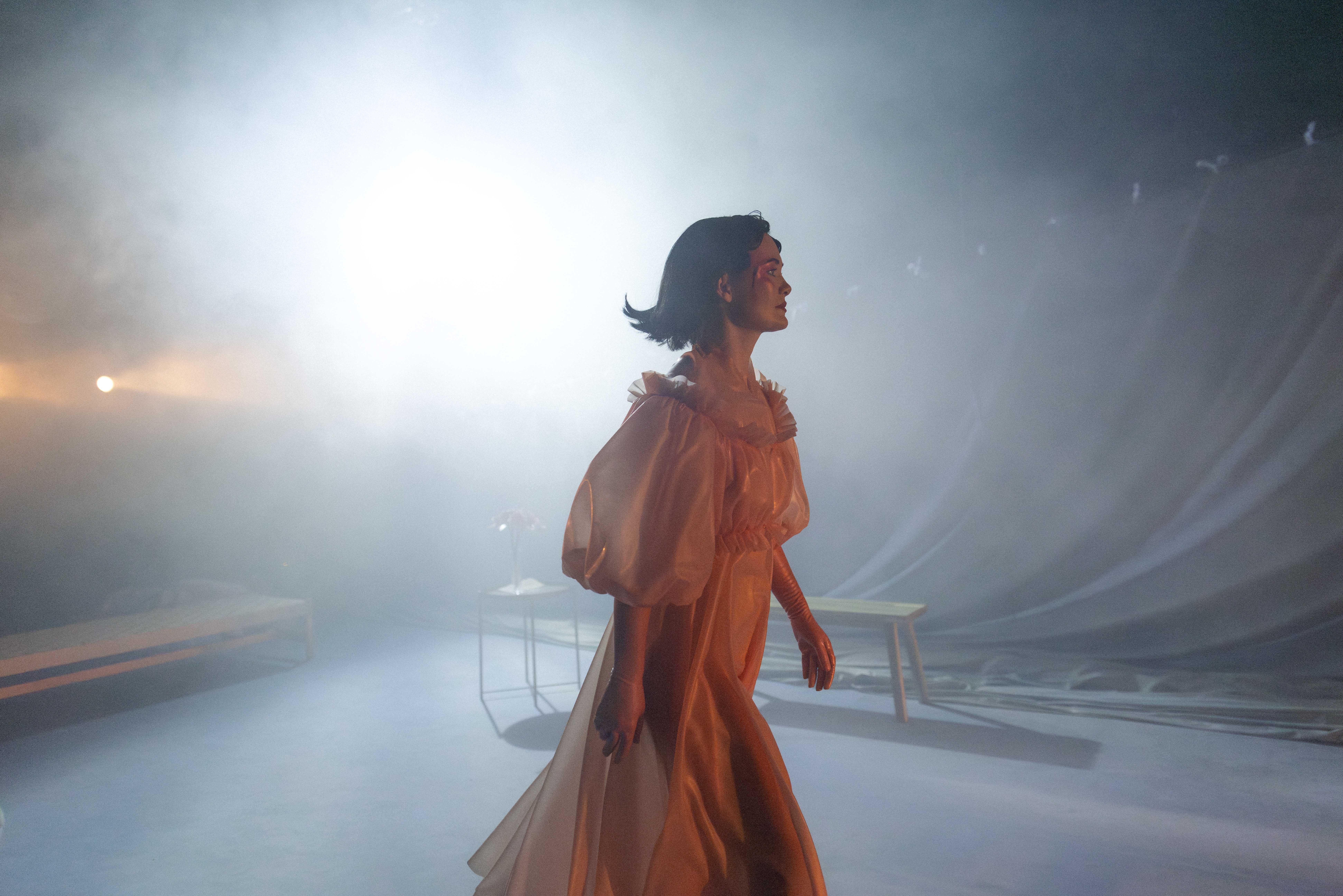 Person i ferskenfarget kjole går gjennom røykfylt scene med sterkt baklys