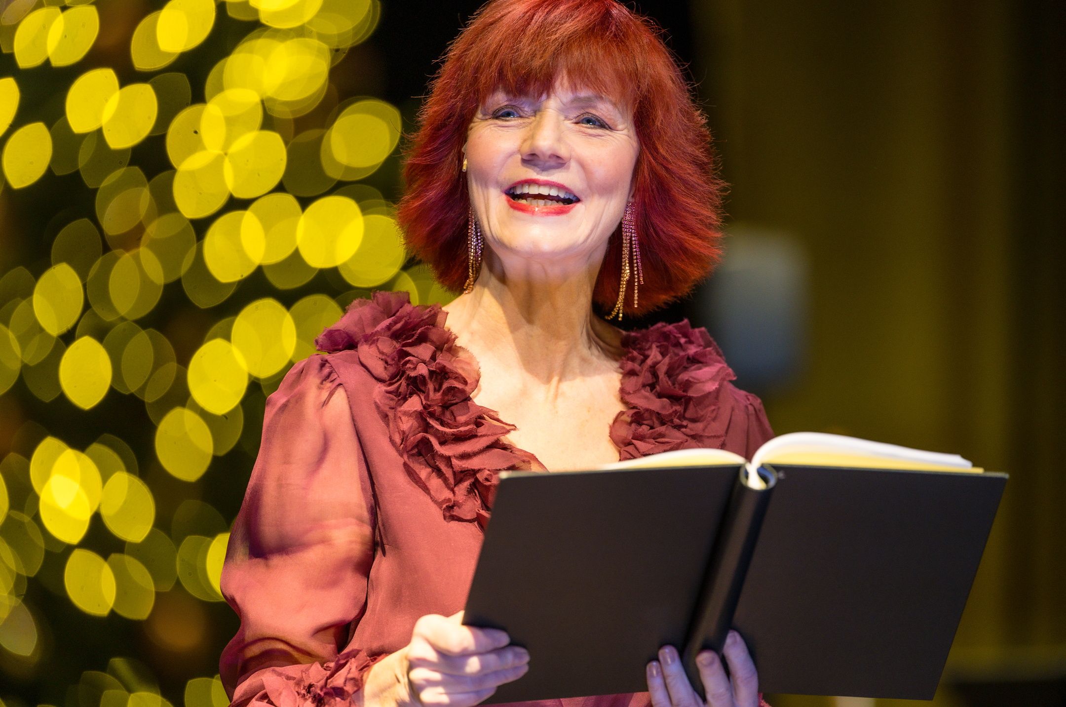 Smilende kvinne med fine klær som holder en bok foran seg